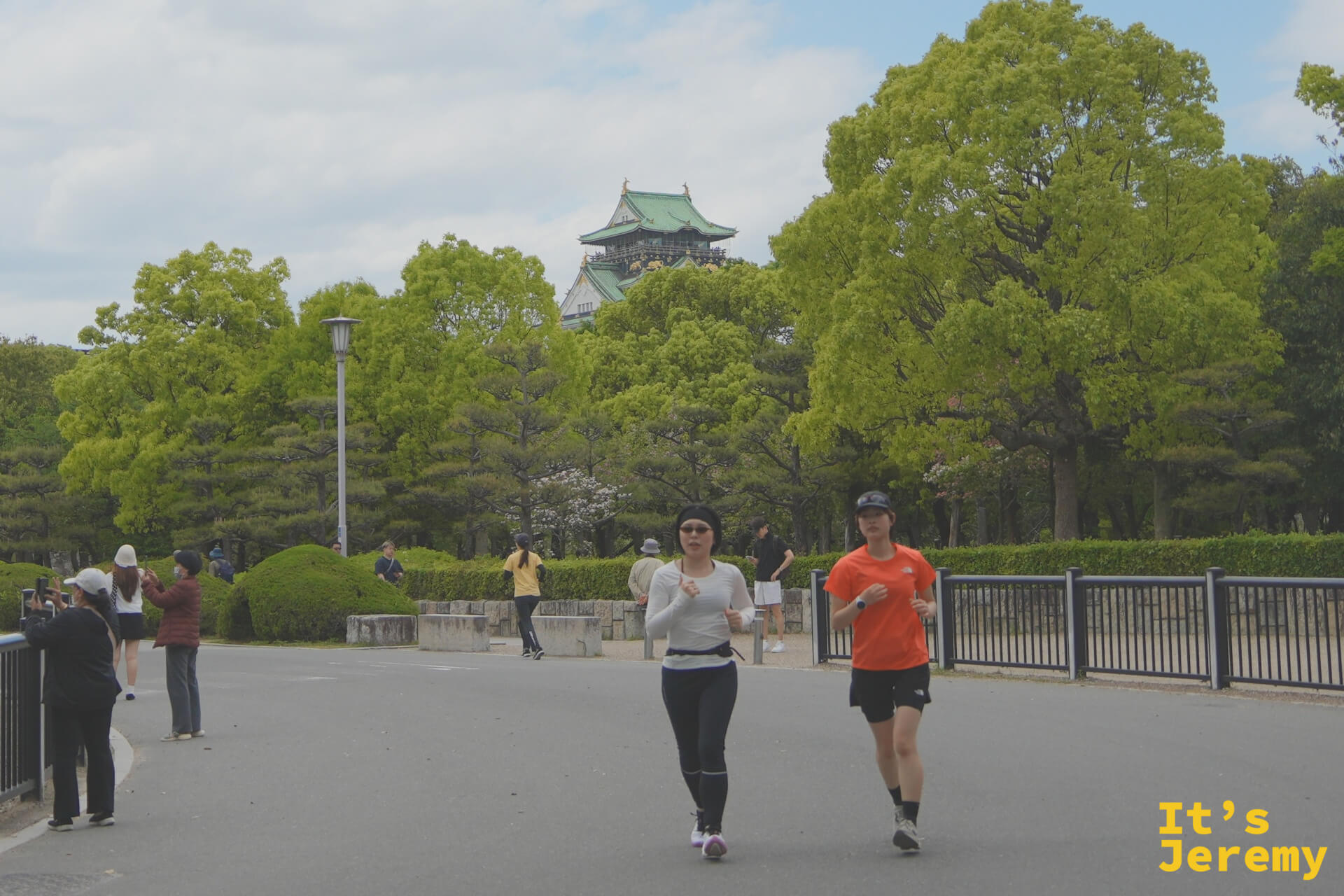 大阪城公園裡,兩名跑者從天守閣背景前跑過,周圍是新綠茂密的大樹