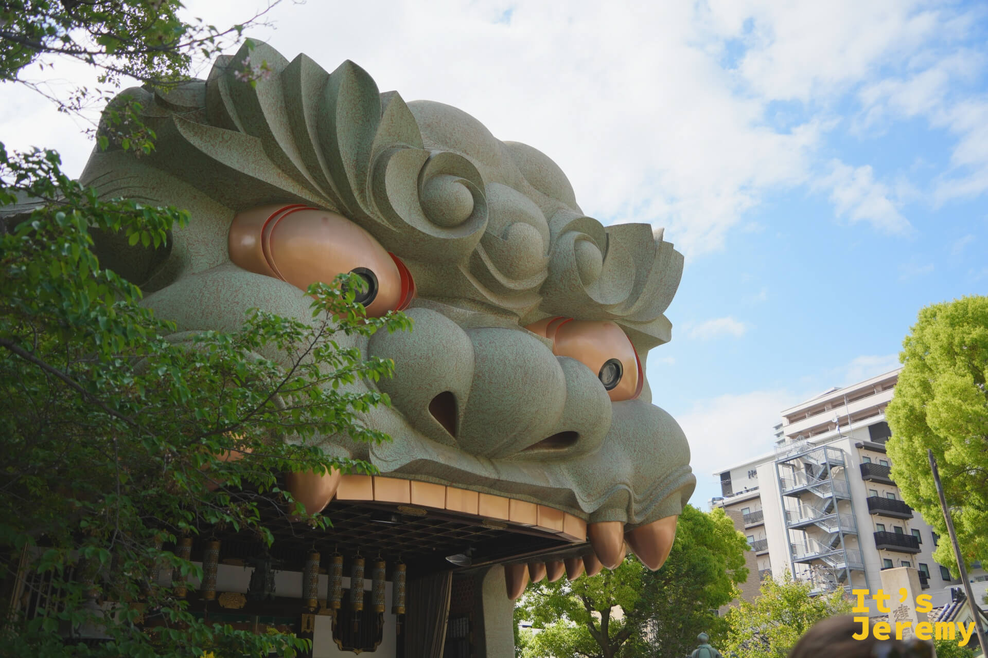 從正面仰角看巨大獅子頭，張口細節與天空形成強烈對比