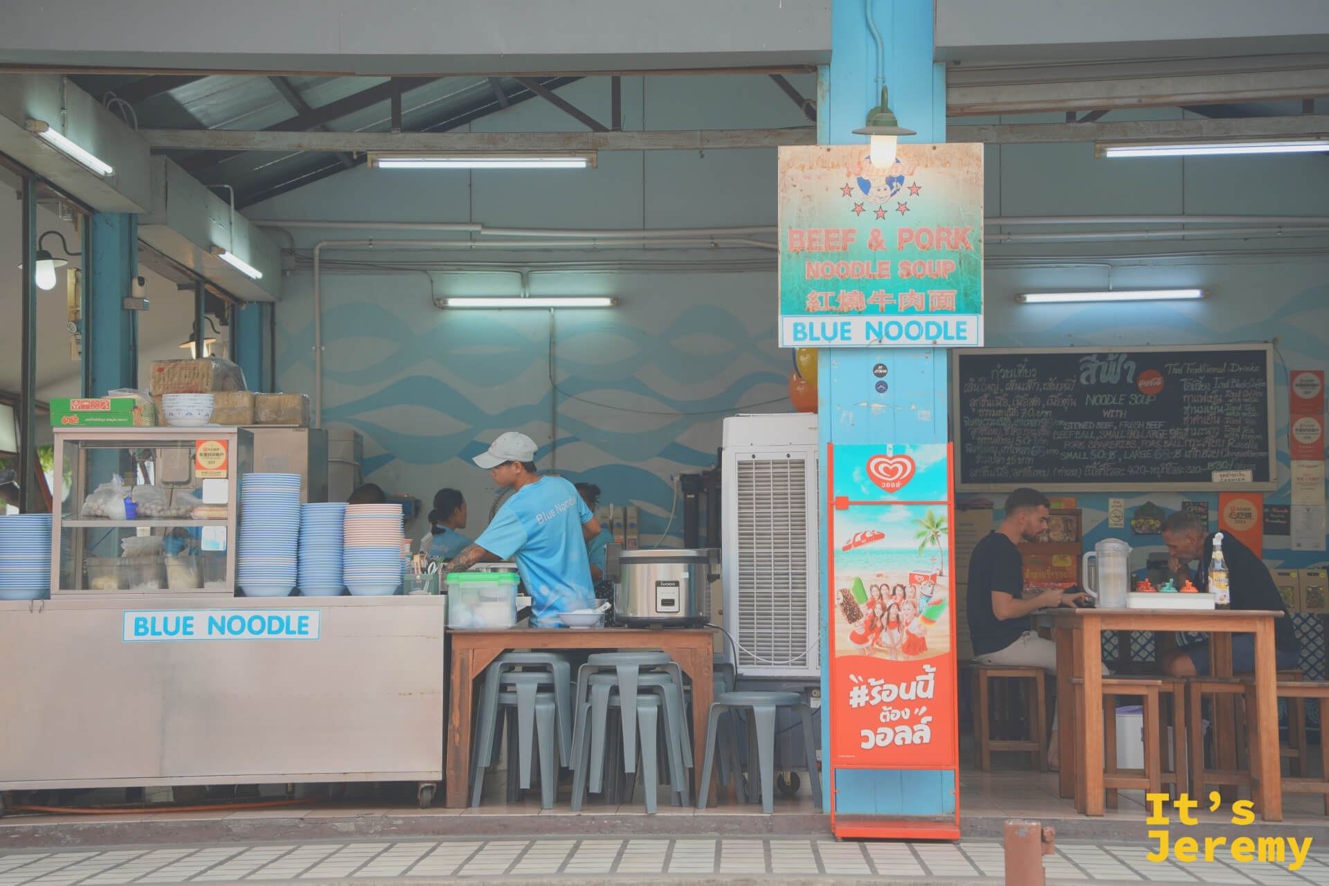 店面外觀，備餐台左側寫著 Blue Noodle，右側客人正在用餐