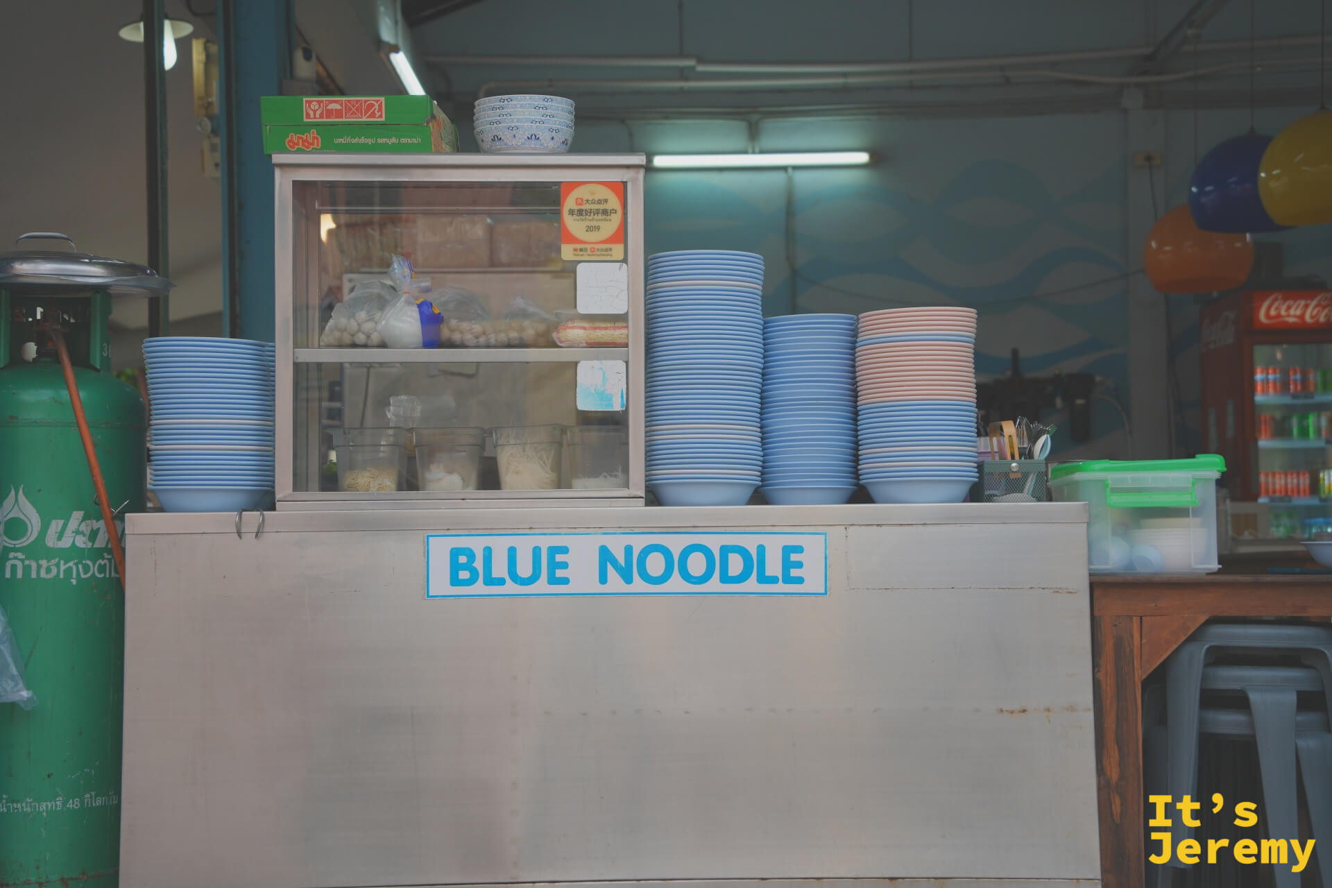 Blue Noodle 備餐台，台面寫著品牌名稱，上方整齊堆放大量藍色與粉色碗盤