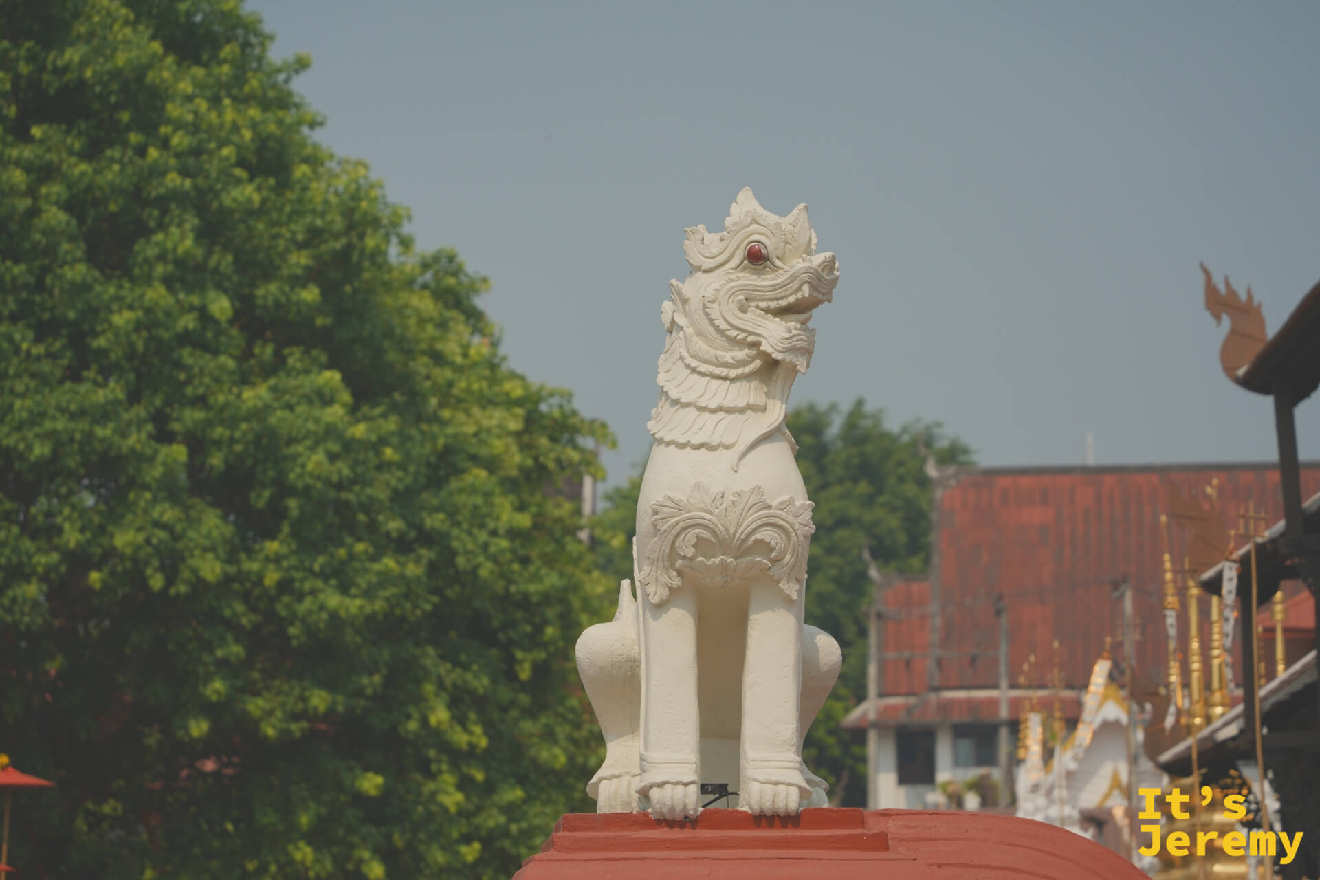 白色獅子守護像（Singha）立於朱紅台座，背景是古城其他寺廟屋頂