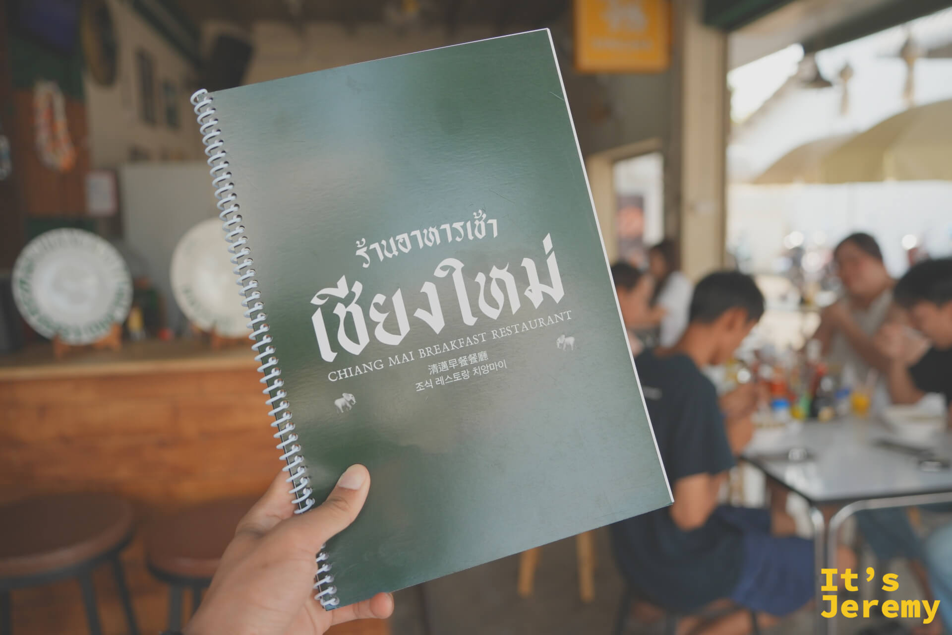 手持 Chiang Mai Breakfast Restaurant 綠色螺旋裝訂菜單本