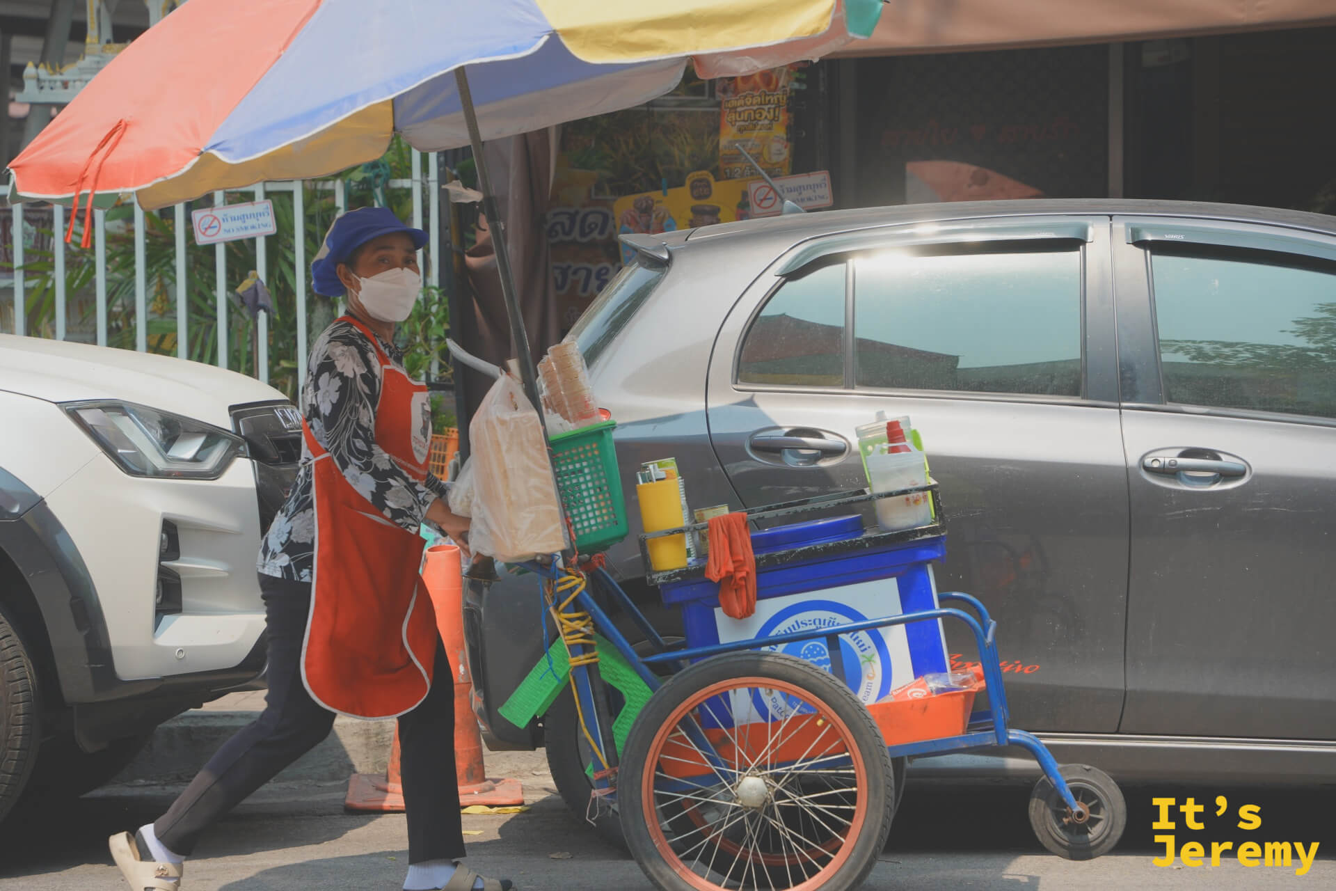 穿紅色圍裙的街頭小販推著三輪餐車,撐一把大傘,走在路上攬客