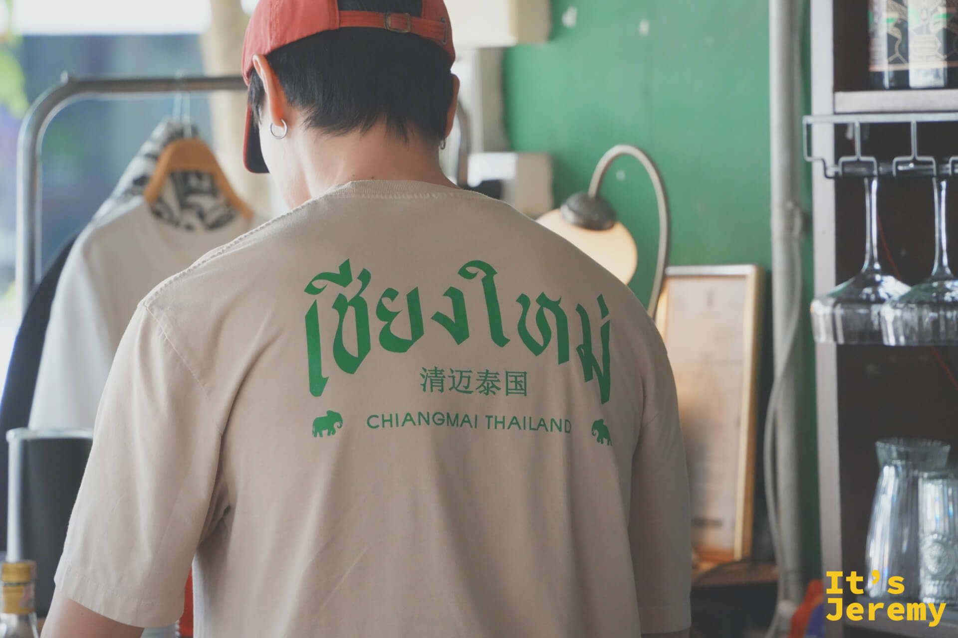 店員戴紅色棒球帽,背對鏡頭,T-shirt 上印有泰文清邁字樣