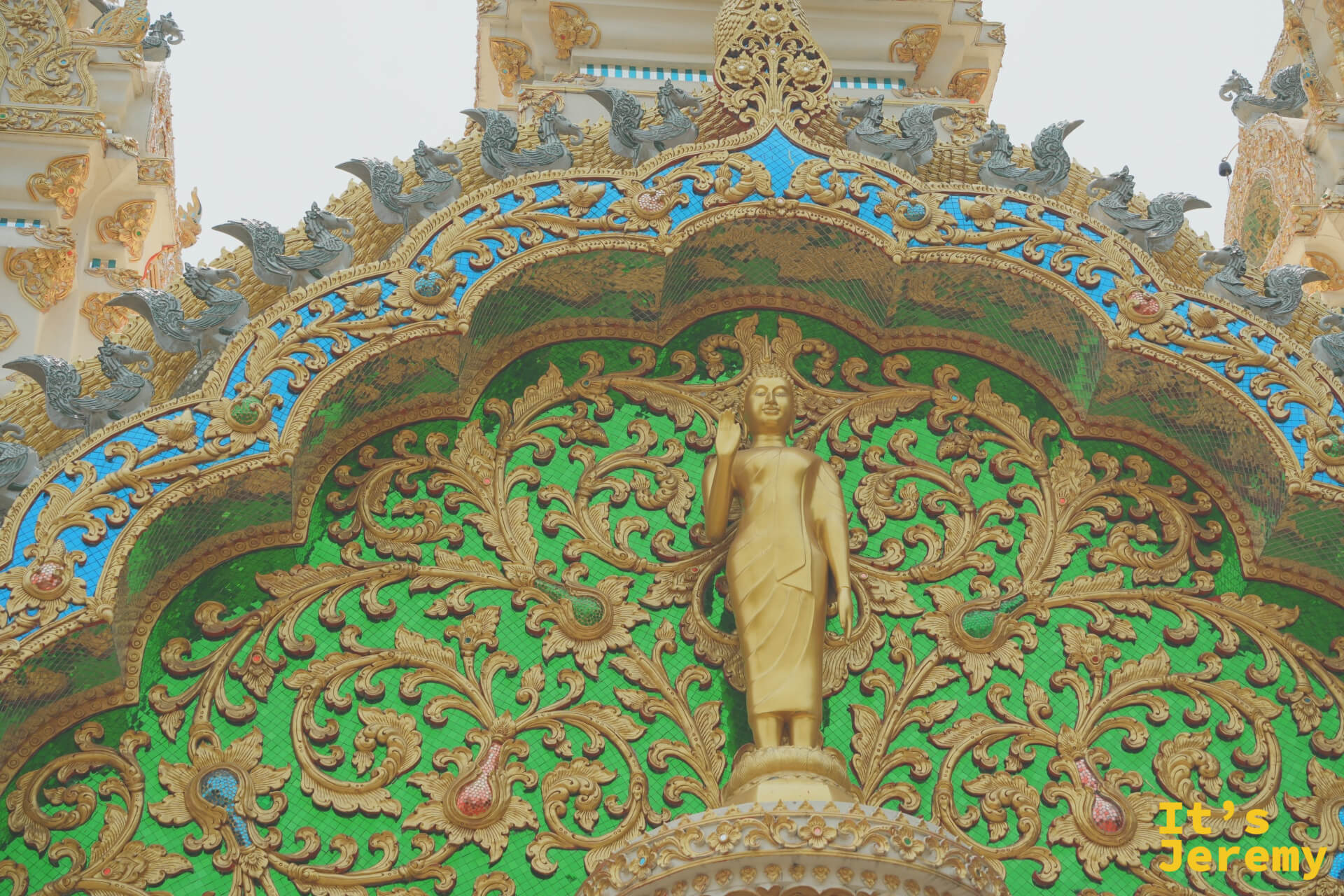 寺廟多尖塔近景，金色立佛嵌於綠底壁龕，塔頂多尖交錯聳立，氣勢宏大