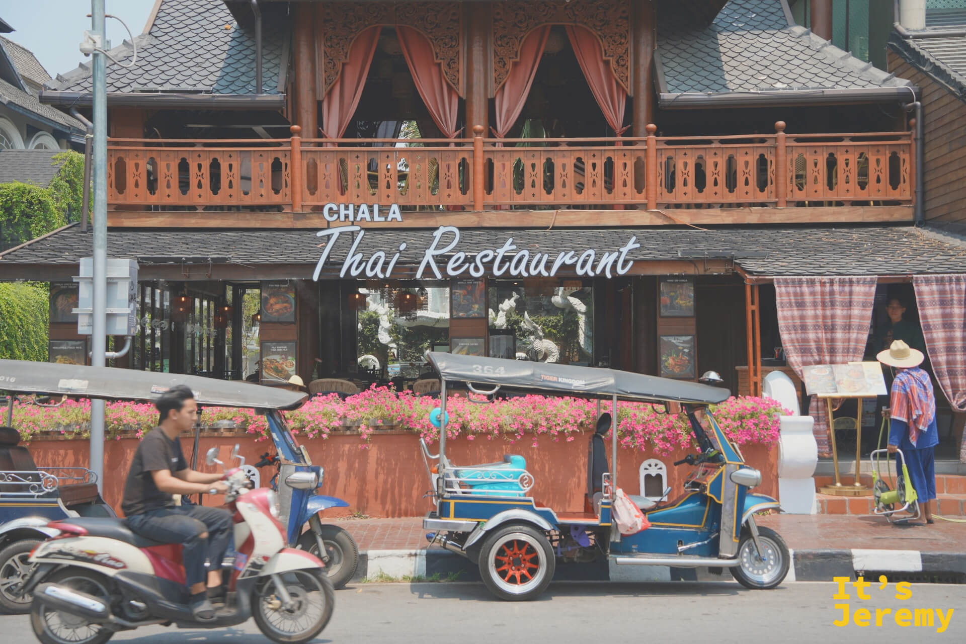 CHALA Thai Restaurant 木造傳統泰式建築外觀,橘紅花叢前停著一輛裝飾嘟嘟車,機車穿越畫面