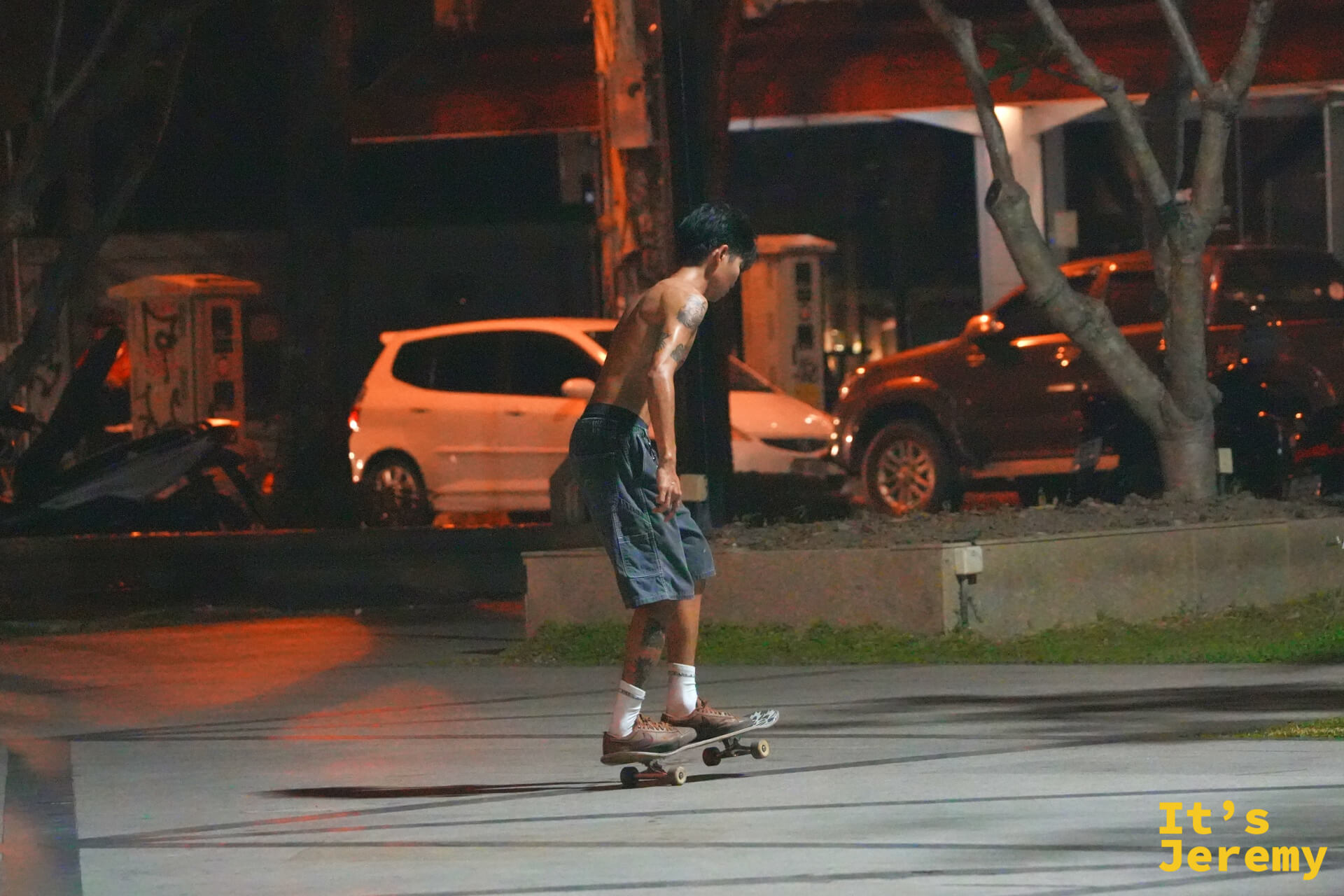 廣場夜間,滑板少年在燈光下練習,身後是停滿車的古城街道
