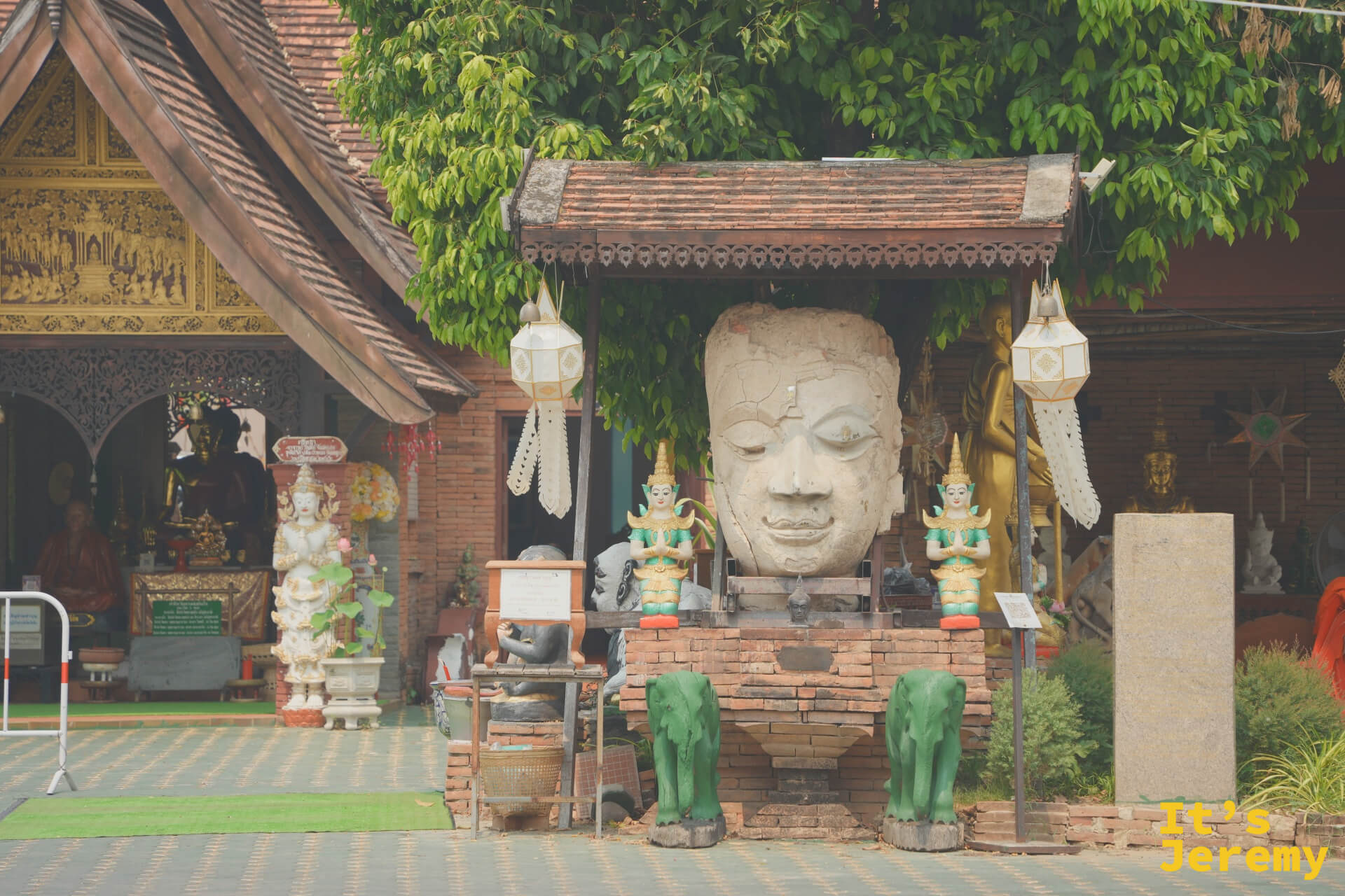 杰林寺的木造廟門與院落全景,兩排翠綠植物夾道,遠方隱約可見古塔與金色立佛