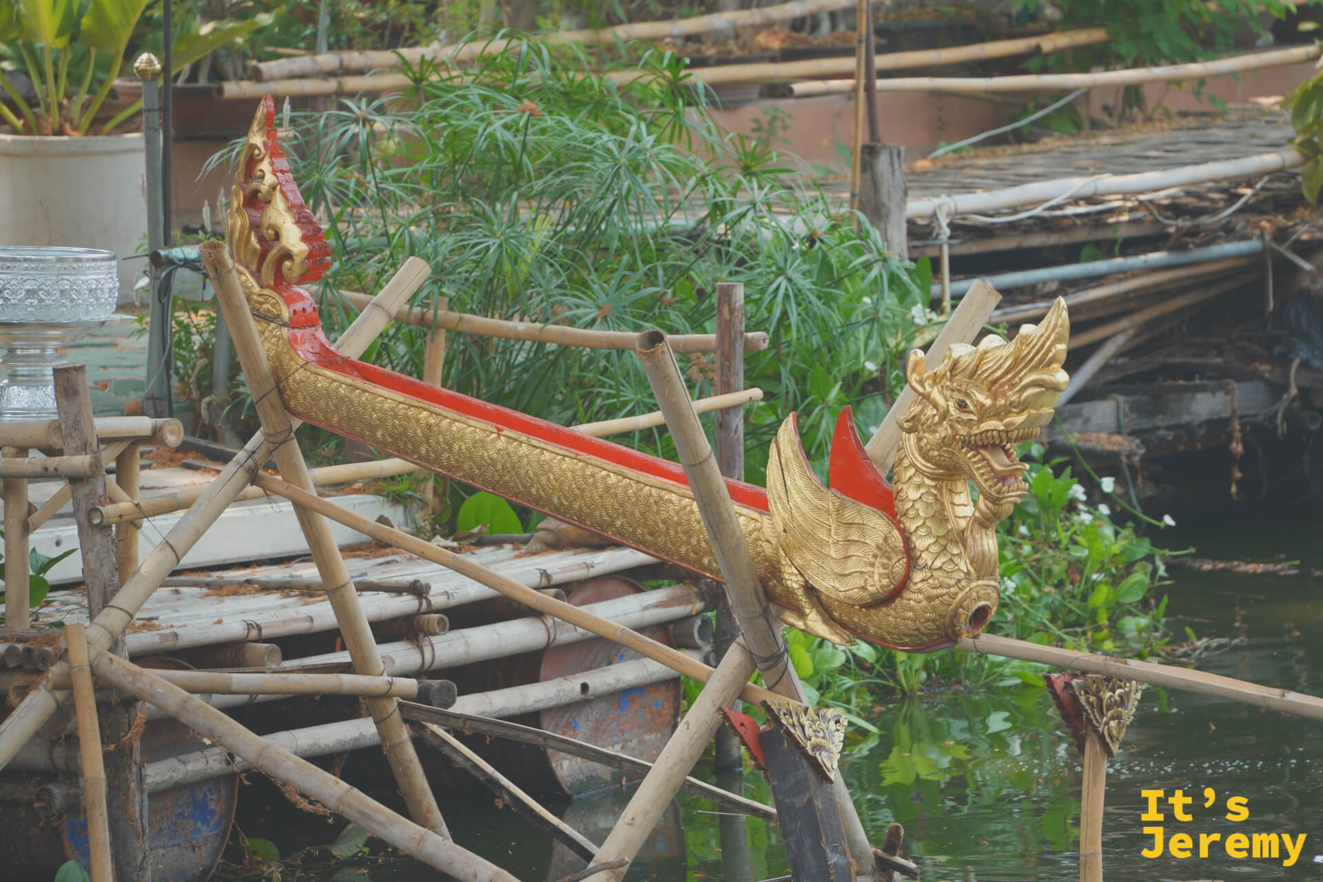 金色那伽龍舟裝飾架立於竹木支架上，頭部張口，旁邊是水道與植栽