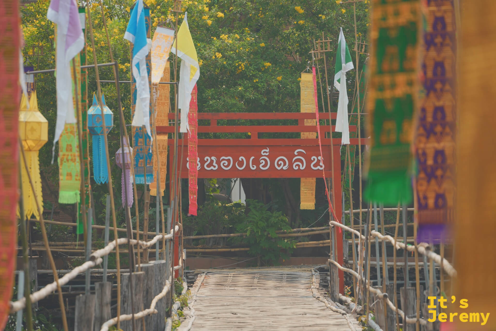 竹橋橫跨七林池，橋頭掛有紅色「หนองเจ็ดลิน」招牌，兩側布滿彩旗與燈籠