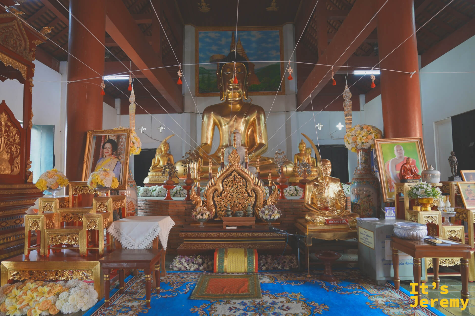 Wat Fon Soi 主殿內部,金色大佛端坐正中央,天頂掛著白色掛燈,地上鋪著藍色地毯,殿內光線昏暗而莊嚴