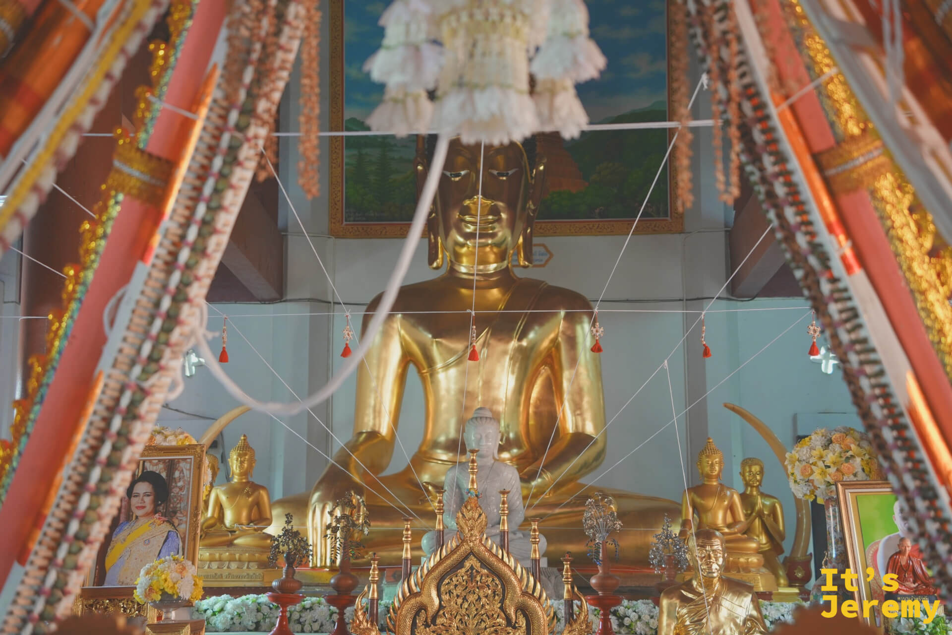 主殿大佛近景，頭頂垂掛白色花狀飾物，主佛兩側各有小型金佛護立，佛台欄杆紋飾繁複細膩