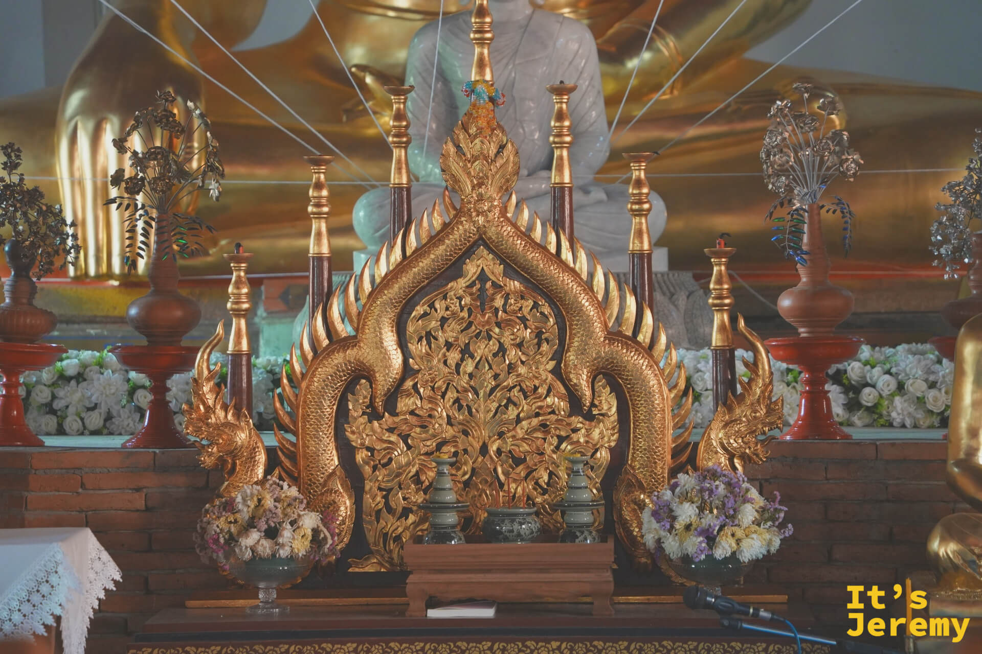 主殿祭台近景，金色那伽雙蛇守護台座兩側，台上供奉小型金佛，周邊花環鮮花點綴，台後可見大型佛像輪廓