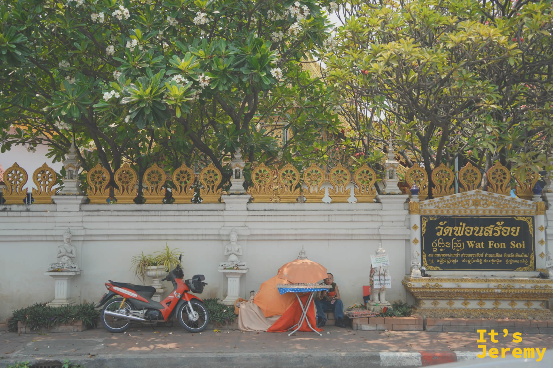 寺廟外牆與入口標示，白牆搭配金色裝飾欄杆，廟名「วัดฟ้อนสร้อย Wat Fon Soi」清晰可見，前方有摩托車停靠，白色雞蛋花樹遮蔭