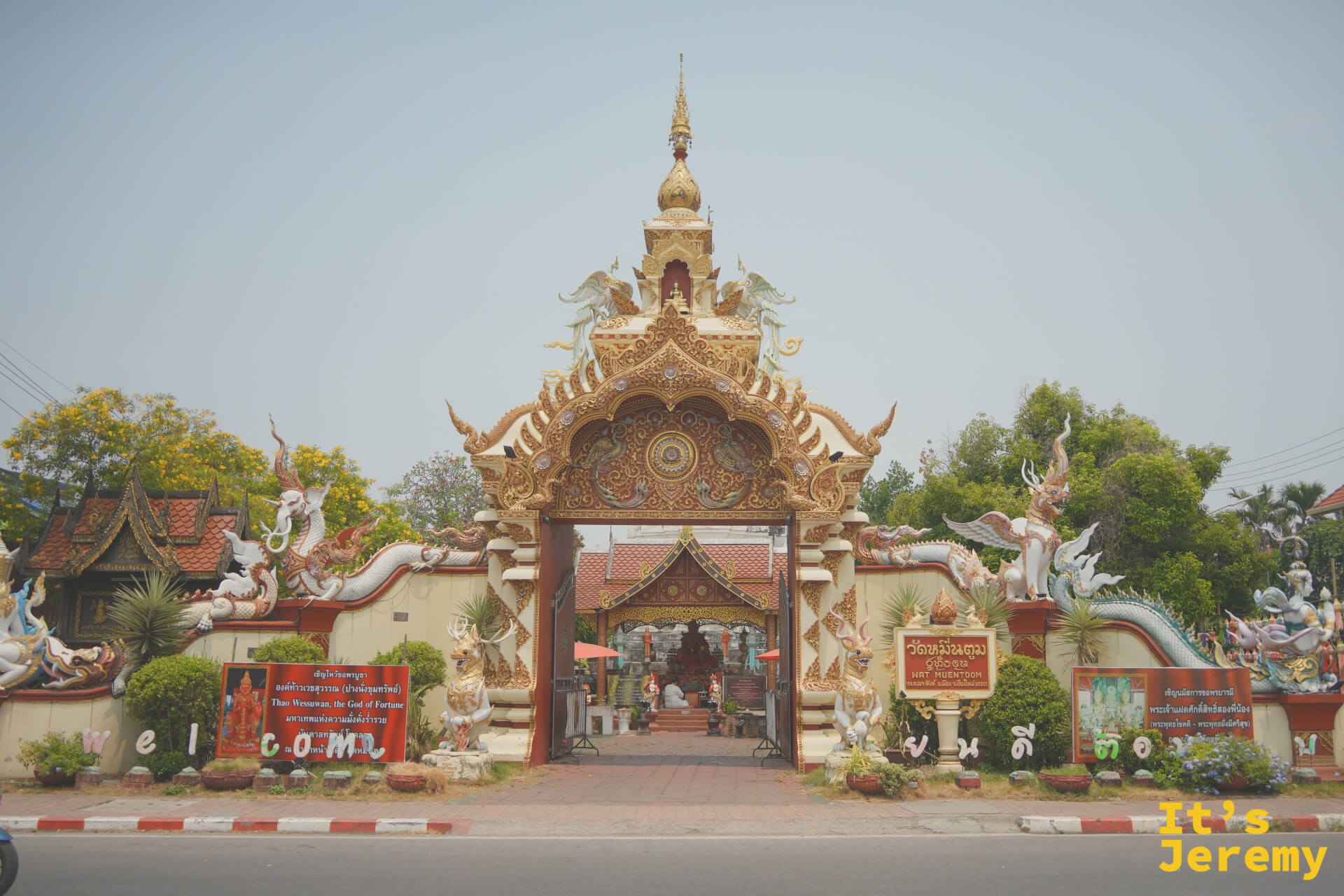 從帕辛路望向 Wat Muentoom 大門,金雕拱頂、那伽蛇身與守護神獸左右相對,門內隱約可見白色古塔