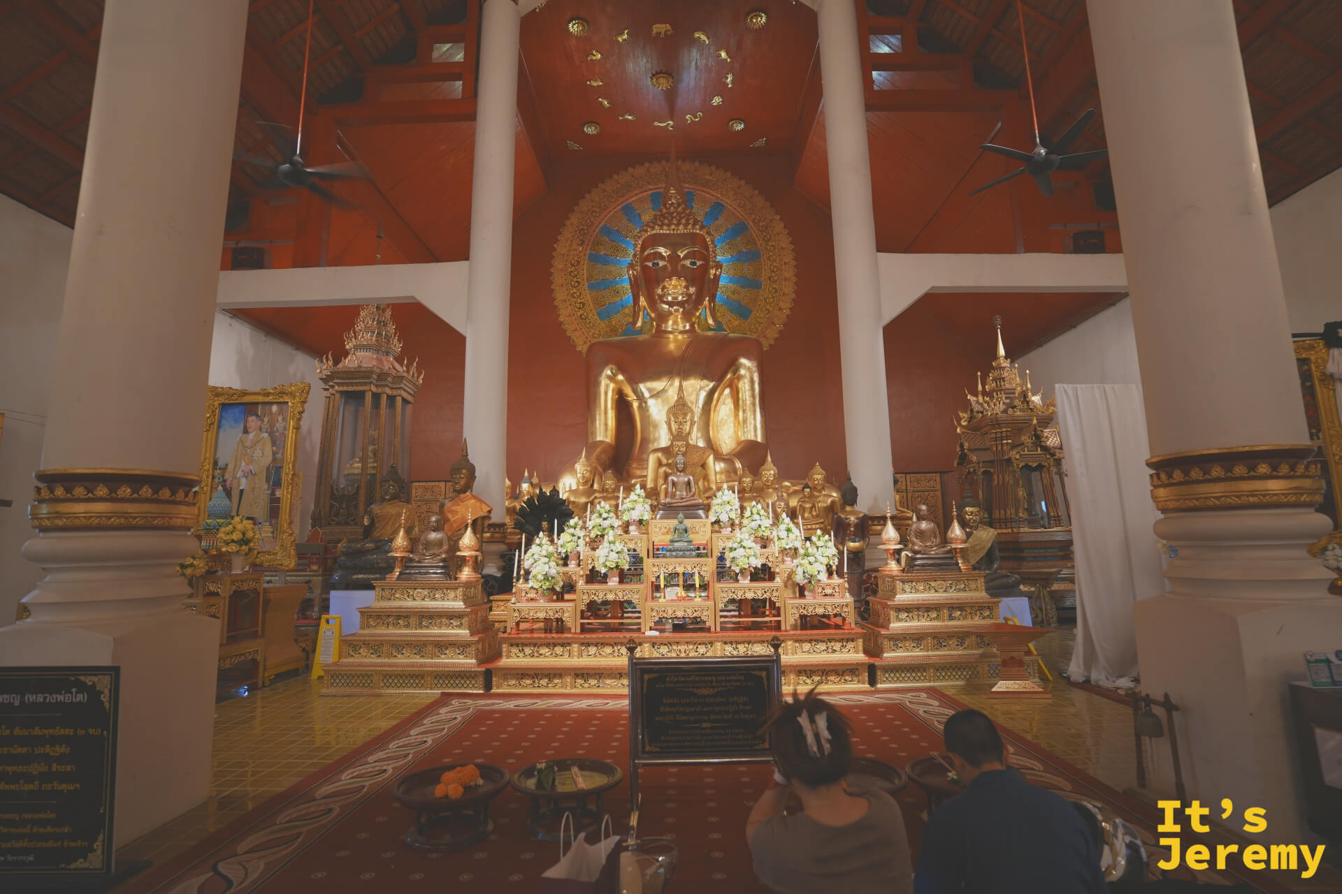 主殿金佛龕近景,信徒跪坐禮拜,佛壇前擺滿花環供品