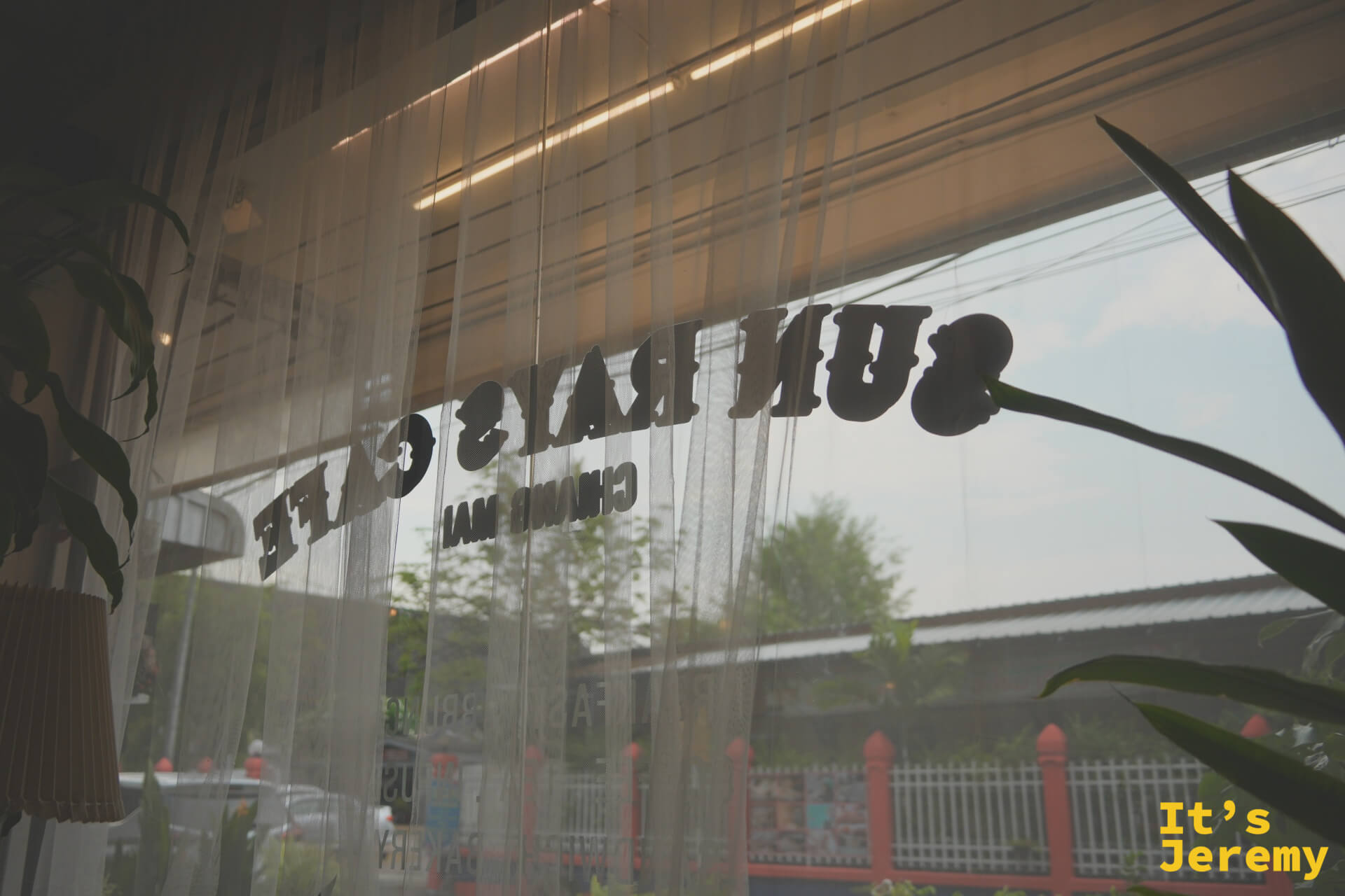 從店內往外看，透過薄紗簾可以看到鏡像的 Sun Rays Café 字樣