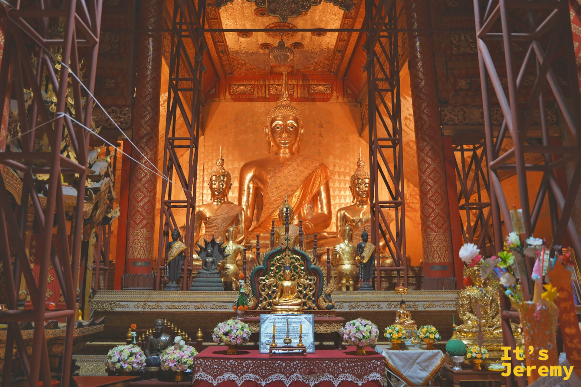 佛堂主佛壇，大型金色坐佛居中，兩側各有侍立佛像，供品花環包圍