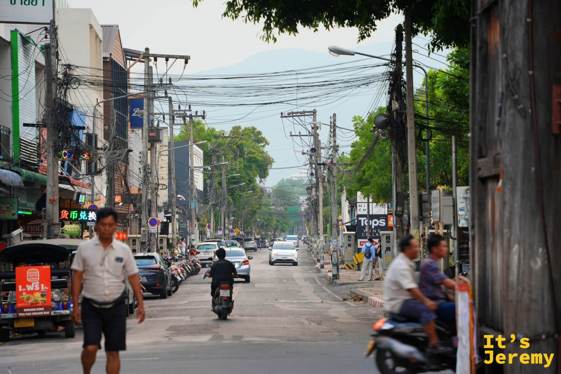 清邡城區主幹道,行人與摩托車共用道路,電線交錯,遠山在城市輪廓後方隱現,是清邡很典型的一幅景