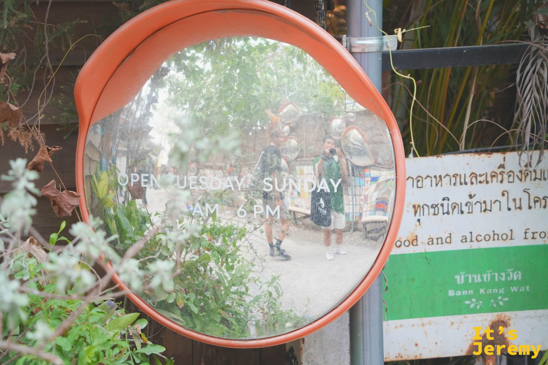 凸面鏡特寫,鏡面上寫著「OPEN TUESDAY SUNDAY AM-6PM」,旁邊綠色看板寫著「บ้านข้างวัด Baan Kang Wat」