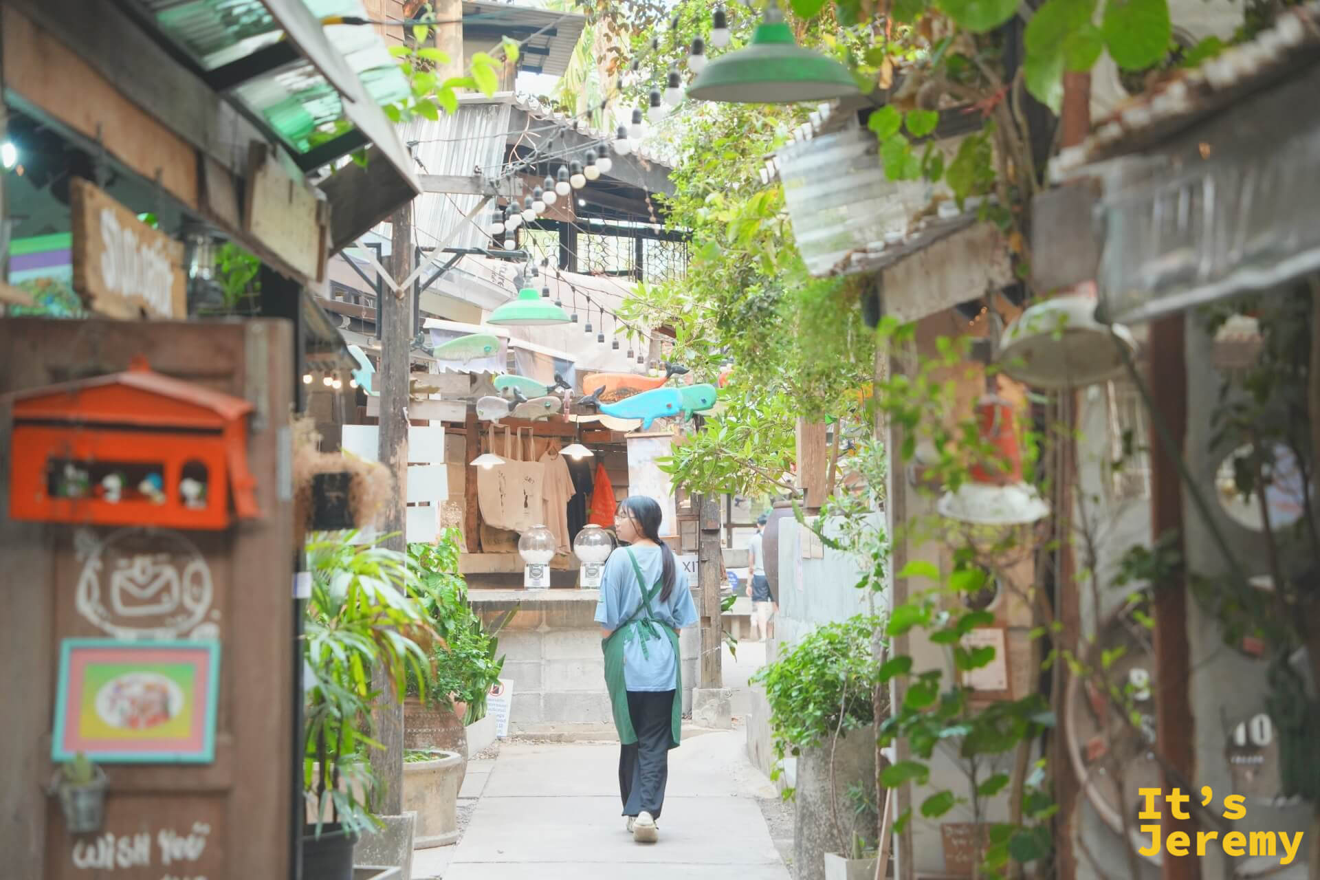 穿圍裙的工作人員走在 Baan Kang Wat 的巷弄間,兩側是藤蔓、植物與各家獨立小店