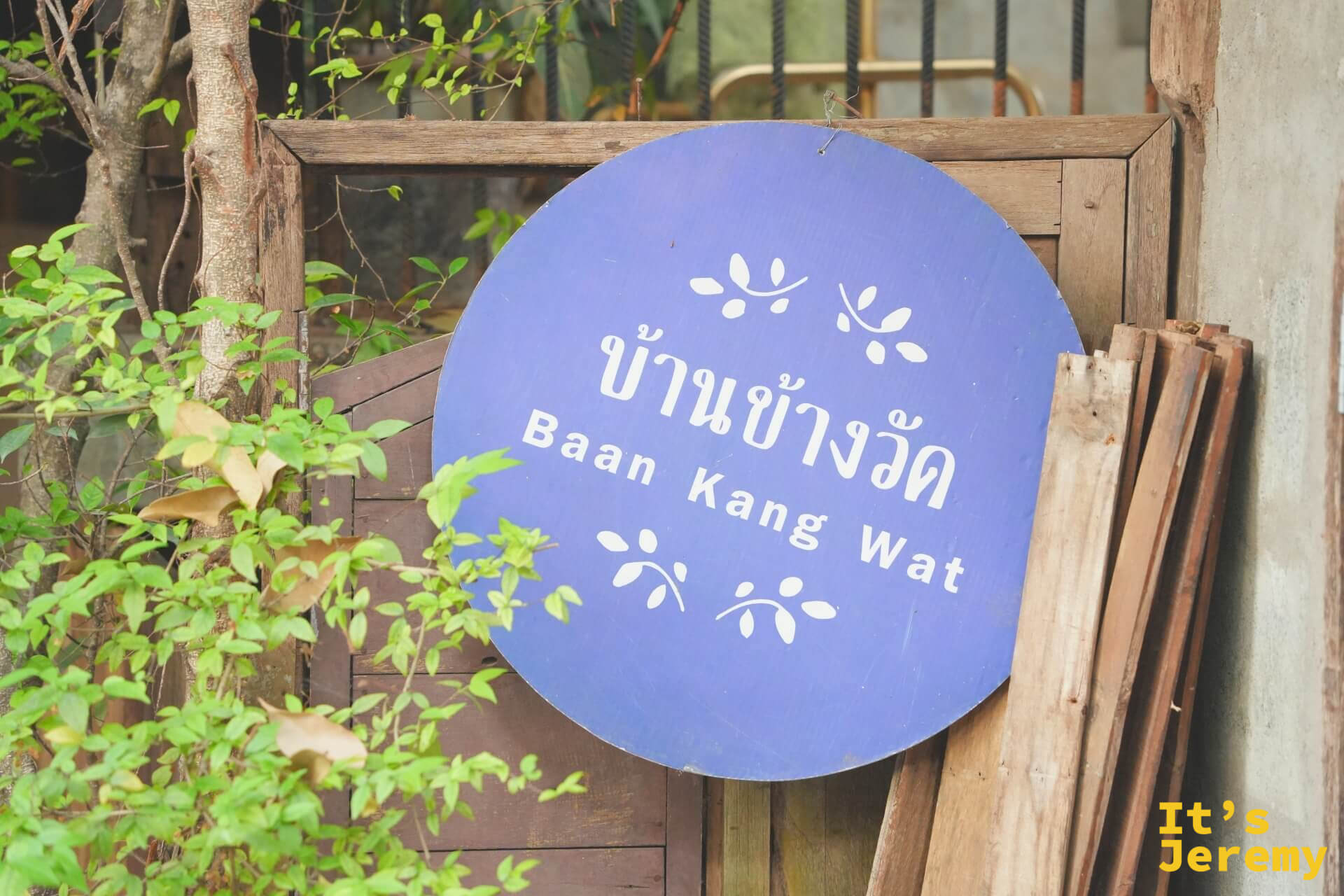 Baan Kang Wat 的藍紫色圓形招牌,泰文 บ้านข้างวัด 下方是英文 Baan Kang Wat