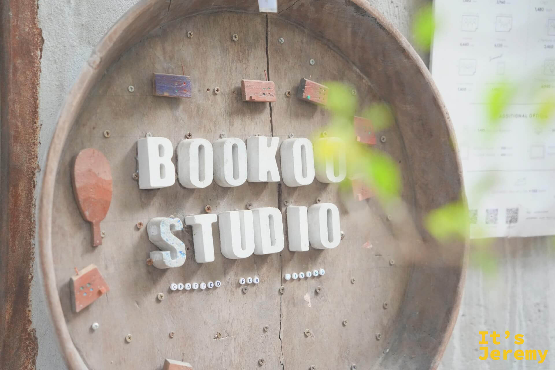 BOOKOO STUDIO 木製圓形招牌近拍,立體白字嵌在舊木桶上,旁邊有小塊彩色木片裝飾
