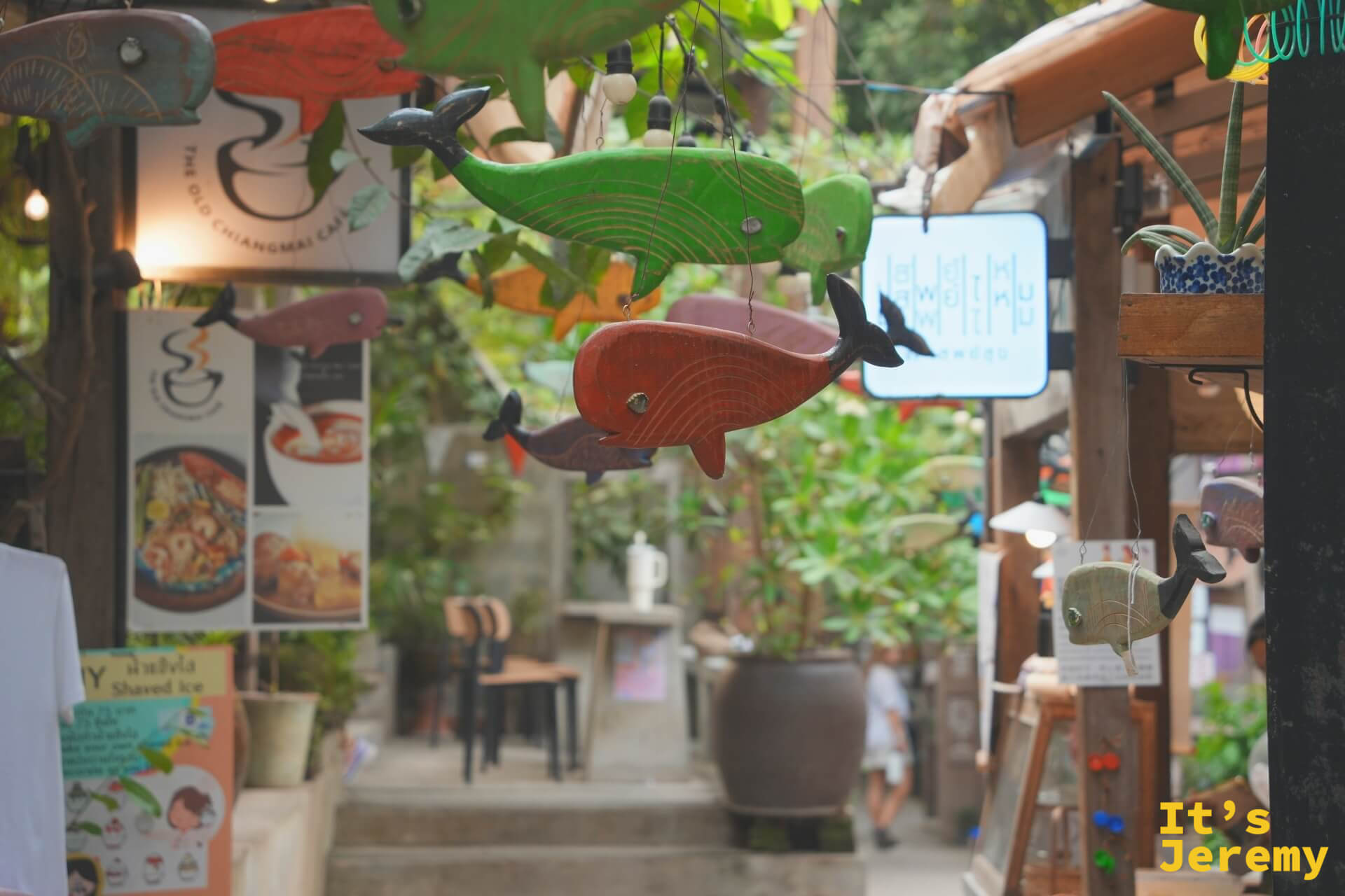 Baan Kang Wat 主要巷弄,天花板掛滿彩色木雕魚,遠方有 The Old Chiangmai Café 招牌
