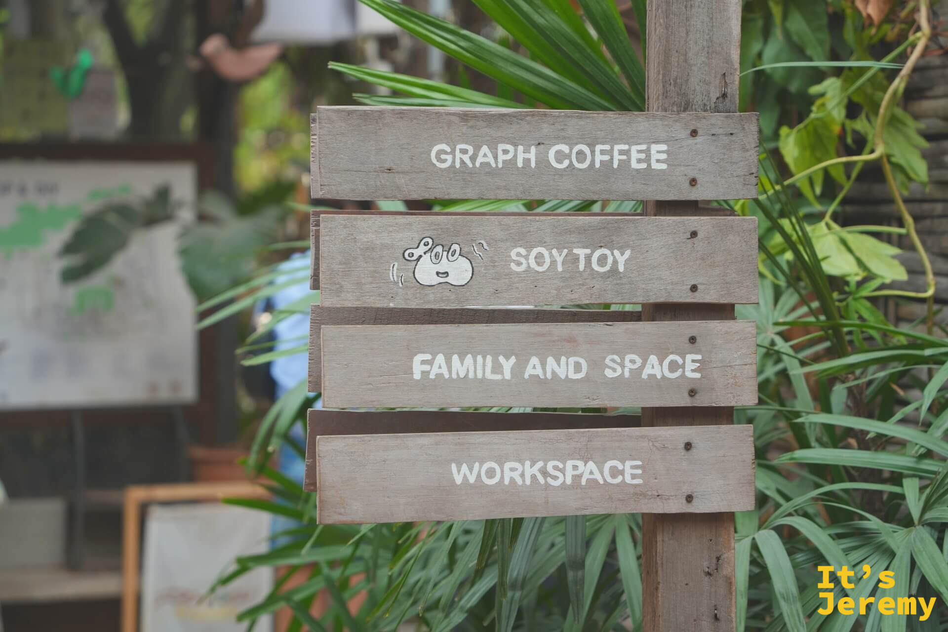 木製指示牌「GRAPH COFFEE / SOY TOY / FAMILY AND SPACE / WORKSPACE」,被綠色植物包圍