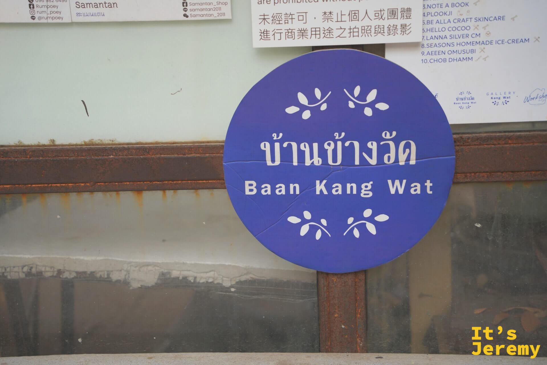 Baan Kang Wat 藍紫色圓形招牌,旁邊牆上有各商店清單與中文禁止商業拍攝告示