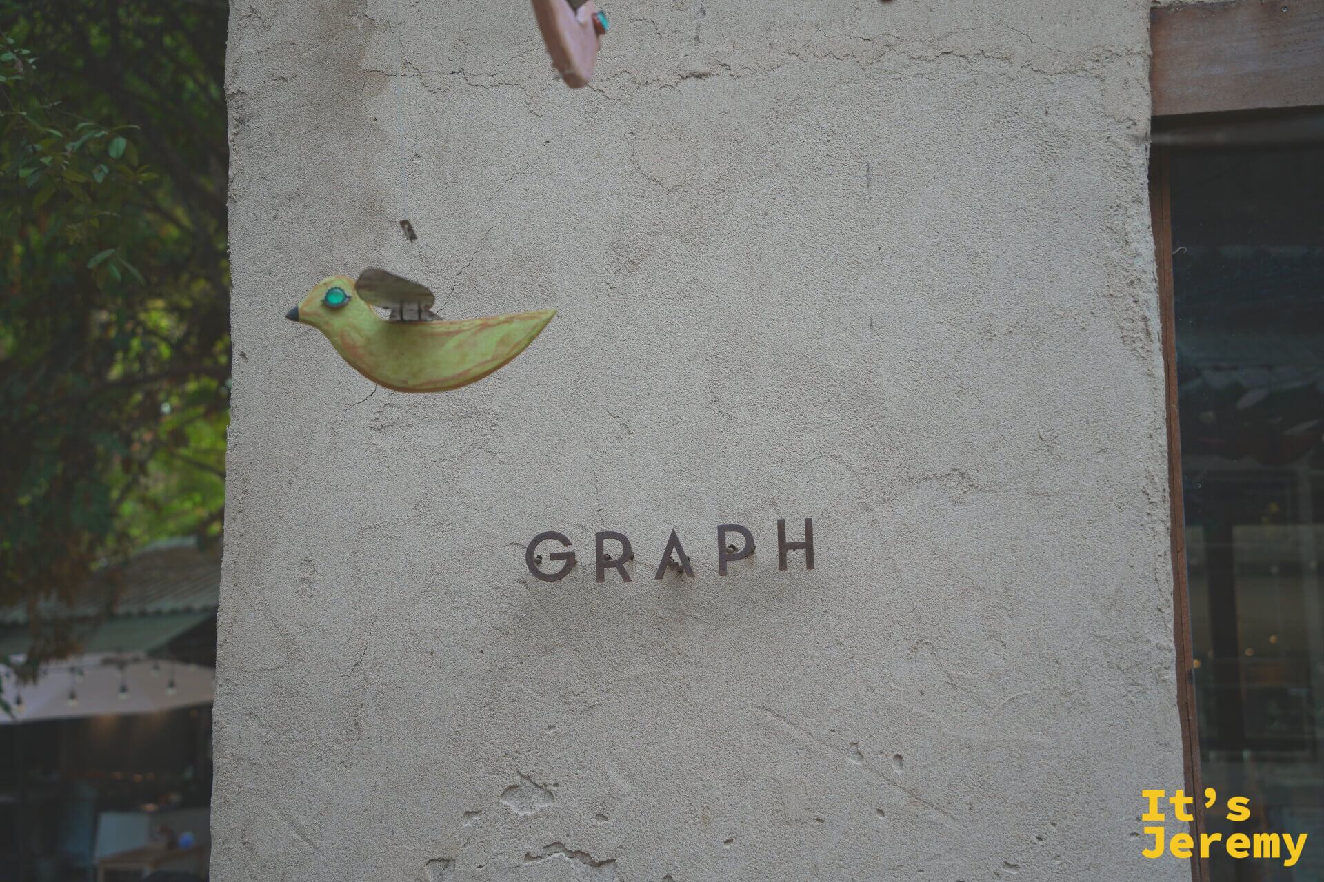 水泥外牆近拍,左側有一隻木雕小鳥裝飾,右側以簡約字體刻著「GRAPH」,風格克制精緻