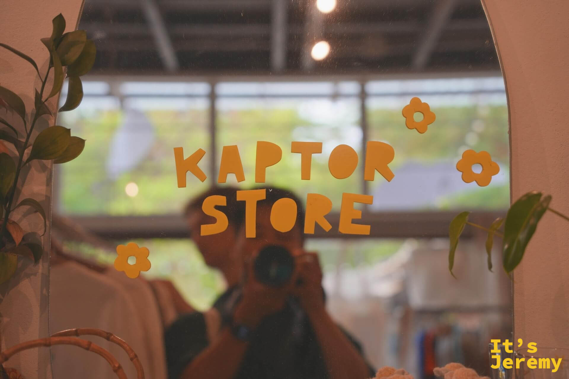 Kaptor Store 鏡子,橘色字母「KAPTOR STORE」貼在拱形鏡面上,搭配小花朵圖案,鏡中倒映著攝影者