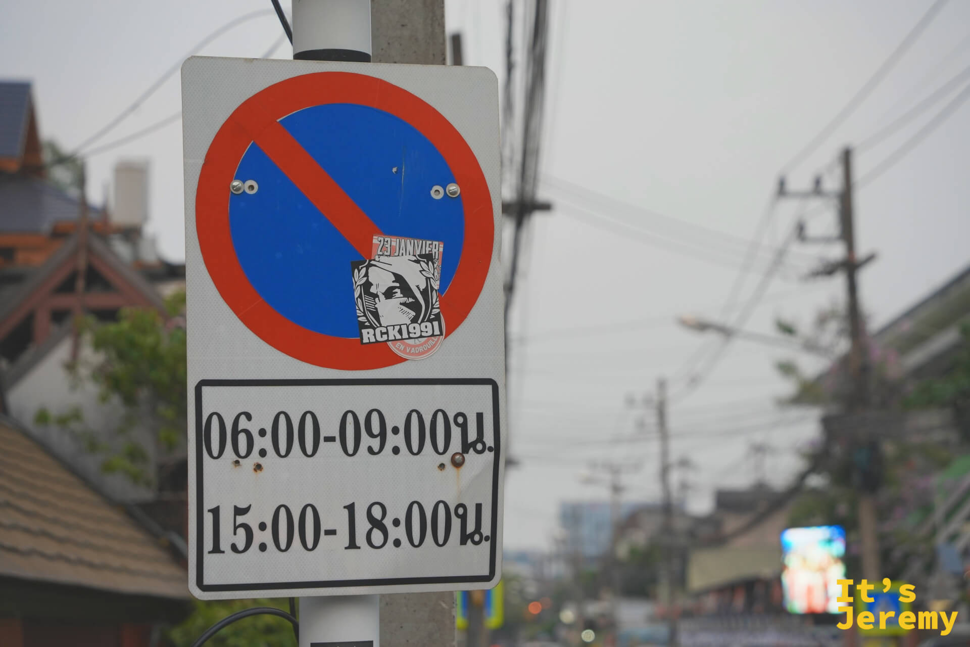 禁止停車標誌上貼著貼紙,後方是清邁街道與交錯的電線