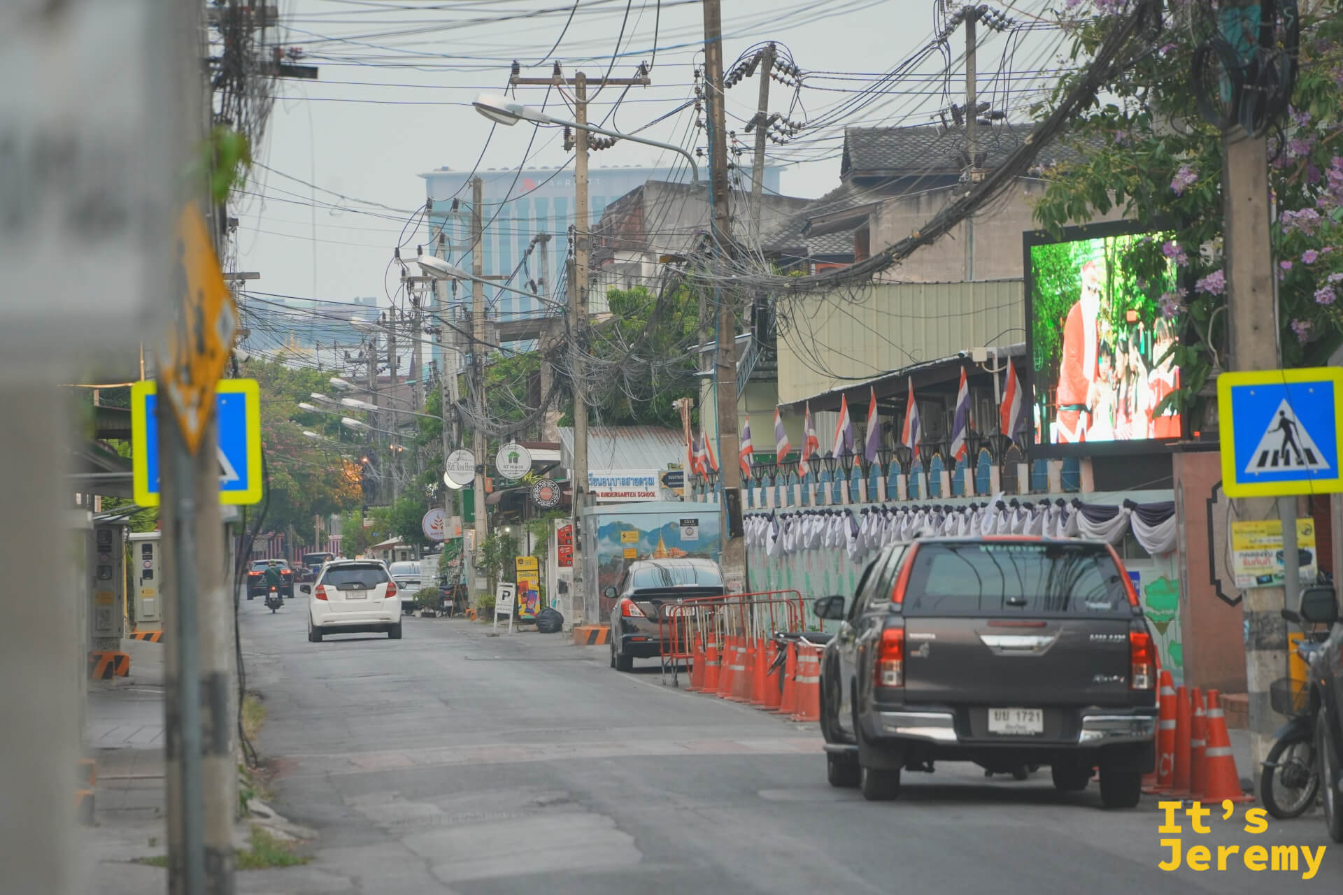掛著一排泰國國旗的街道,深色皮卡車停在橘色三角錐旁