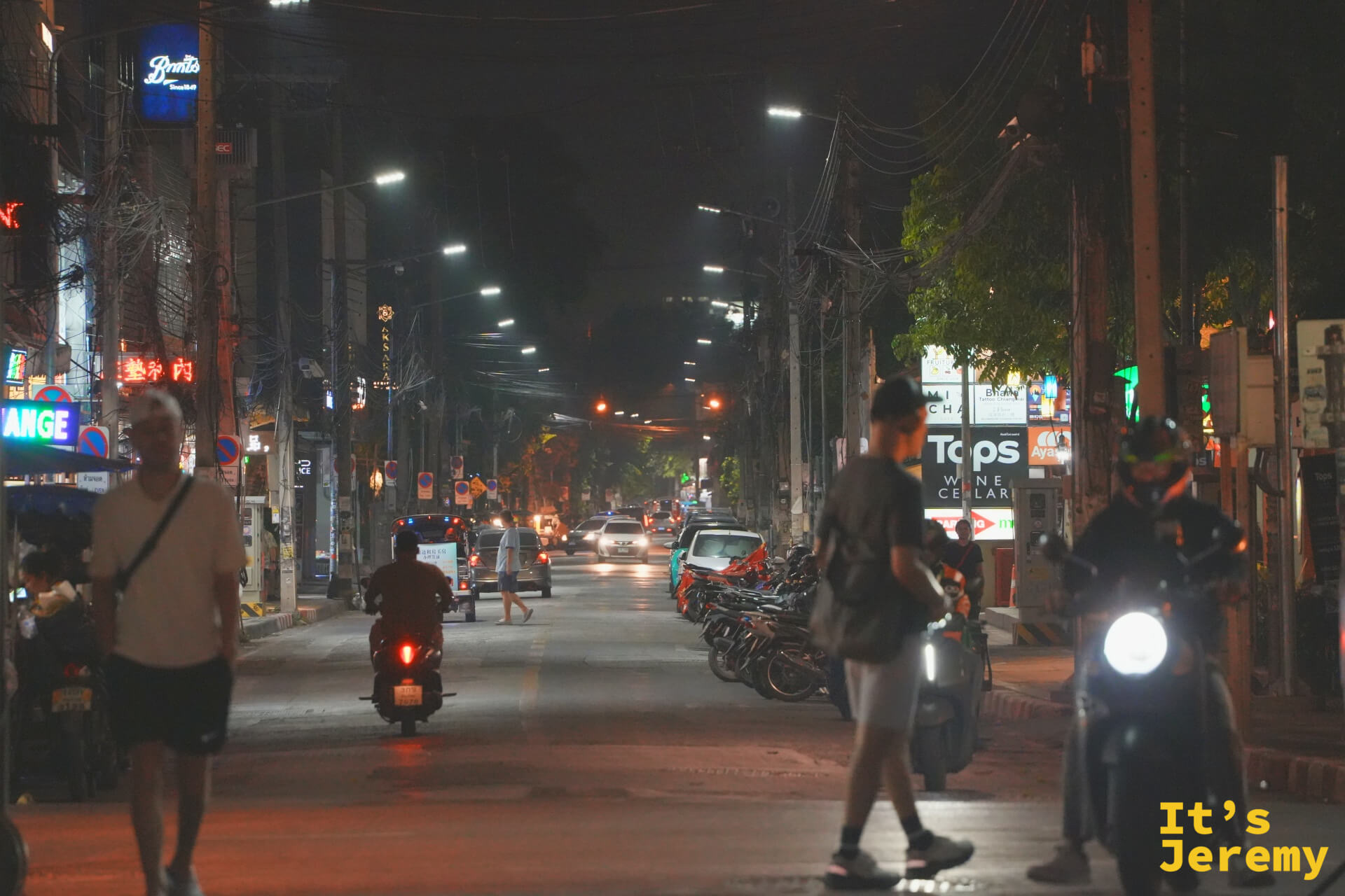 入夜的街道,行人與摩托車在路燈下交錯,兩側招牌亮起