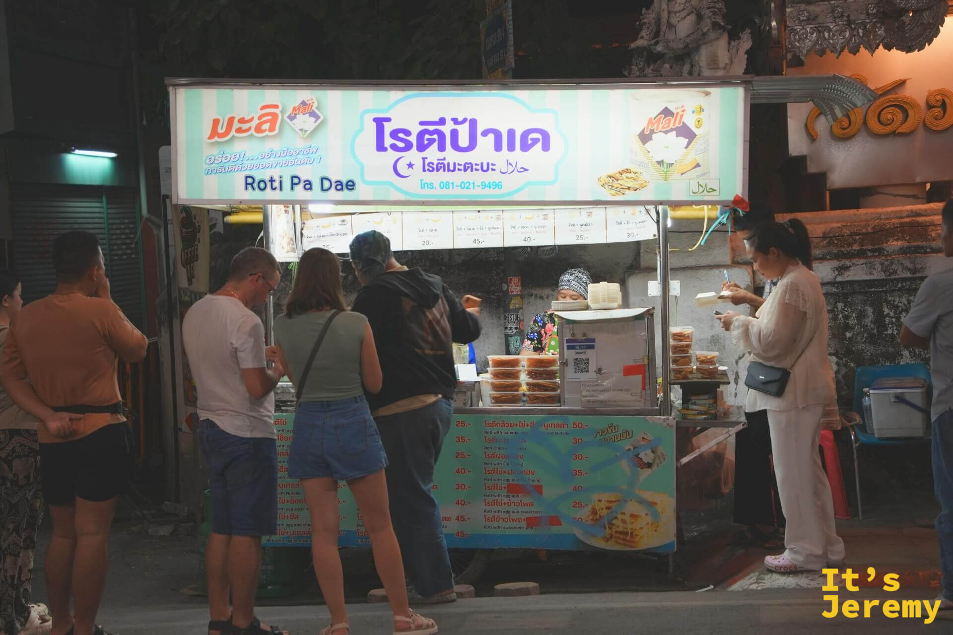 Roti Pa Dae 攤車正面，薄荷綠招牌寫著泰文店名與電話，攤前站滿等餐的客人