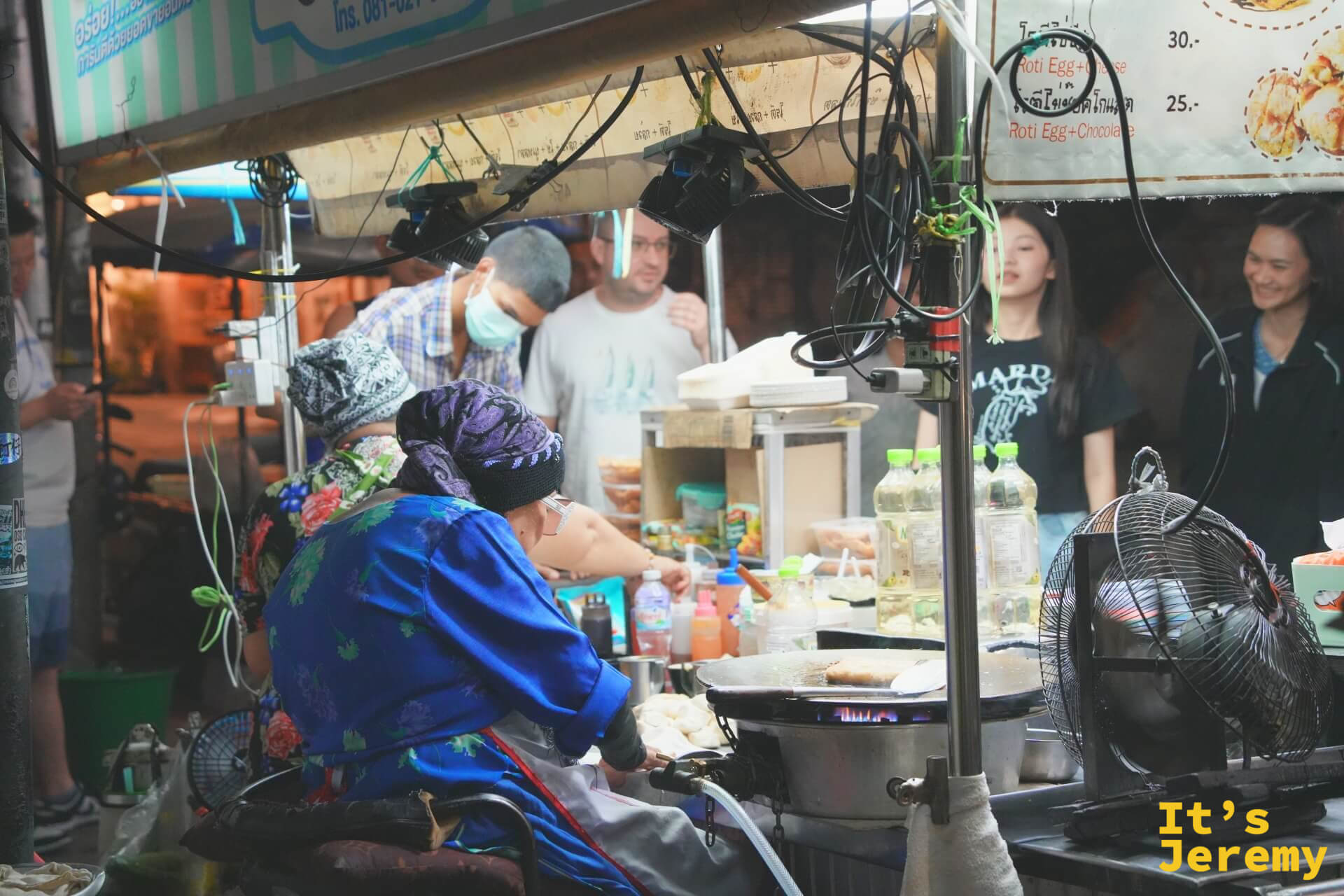 攤位側面視角：奶奶坐在鐵板前工作，攤外圍著等餐與拍照的客人