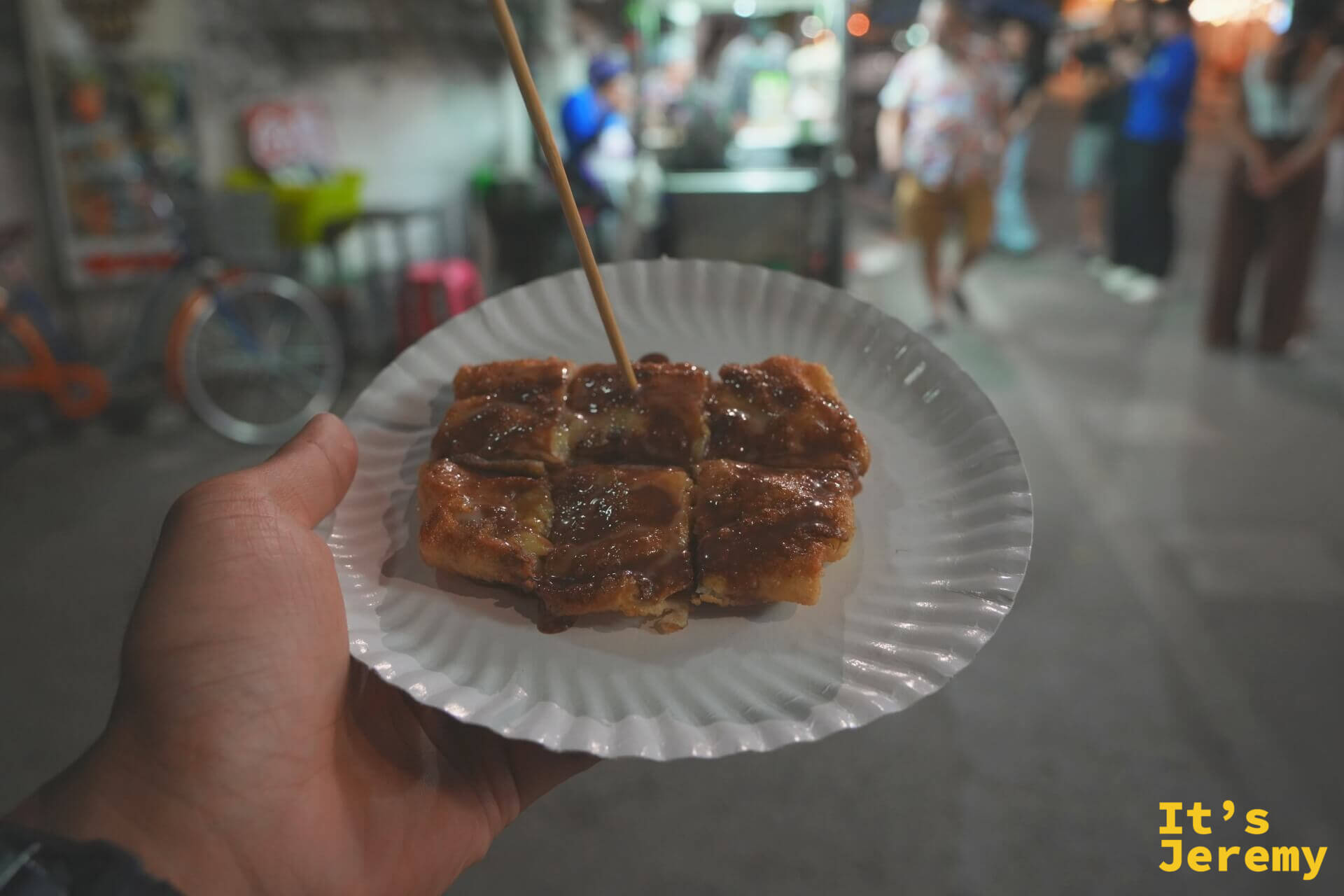成品：紙盤上切成塊狀的香蕉羅蒂淋滿 Nutella，插著竹籤，背景是夜裡的街道