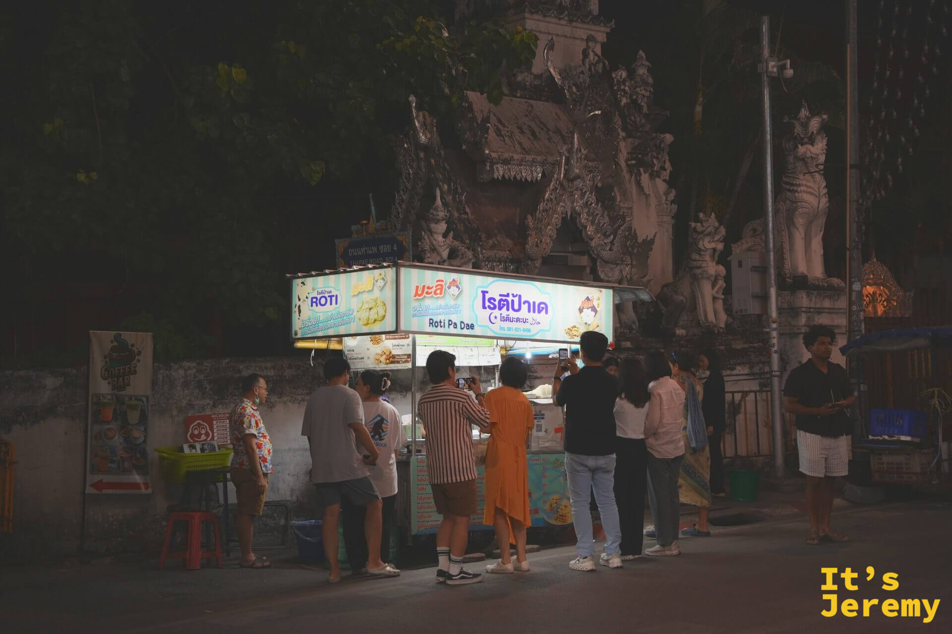 夜裡的 Roti Pa Dae 攤車亮著燈，停在白色寺廟山門前，門前已聚集排隊人潮