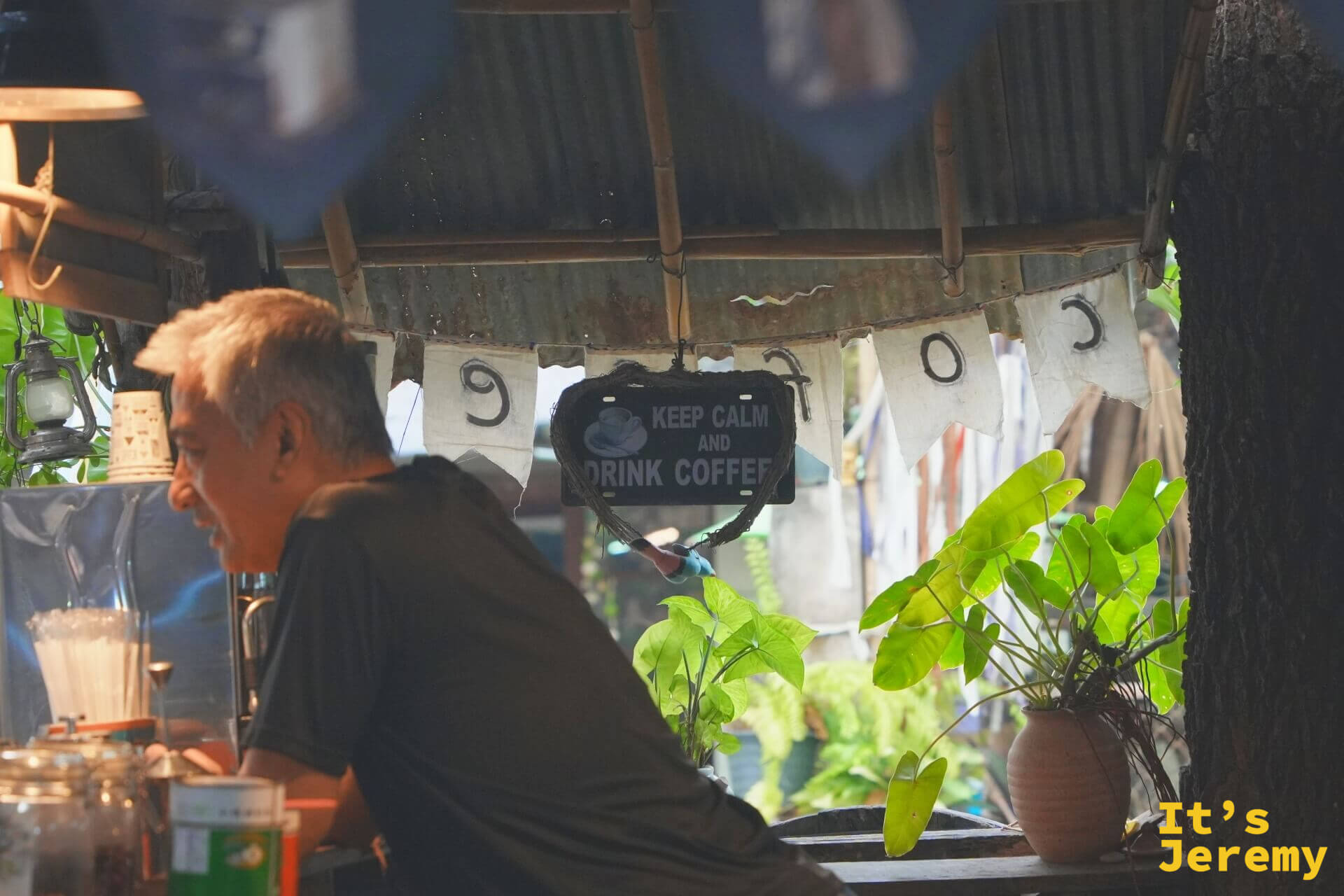 咖啡攤的大叔在攤位裡備料,頭頂掛著「KEEP CALM AND DRINK COFFEE」的牌子