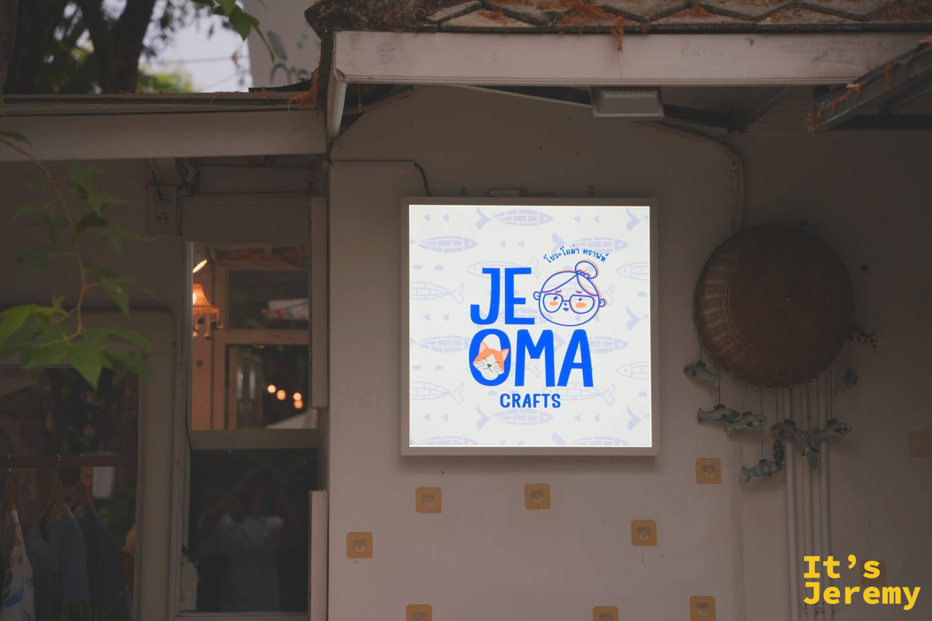 JE OMA CRAFTS 的方形燈箱招牌,藍色字體配戴眼鏡奶奶與貓咪的插畫 logo