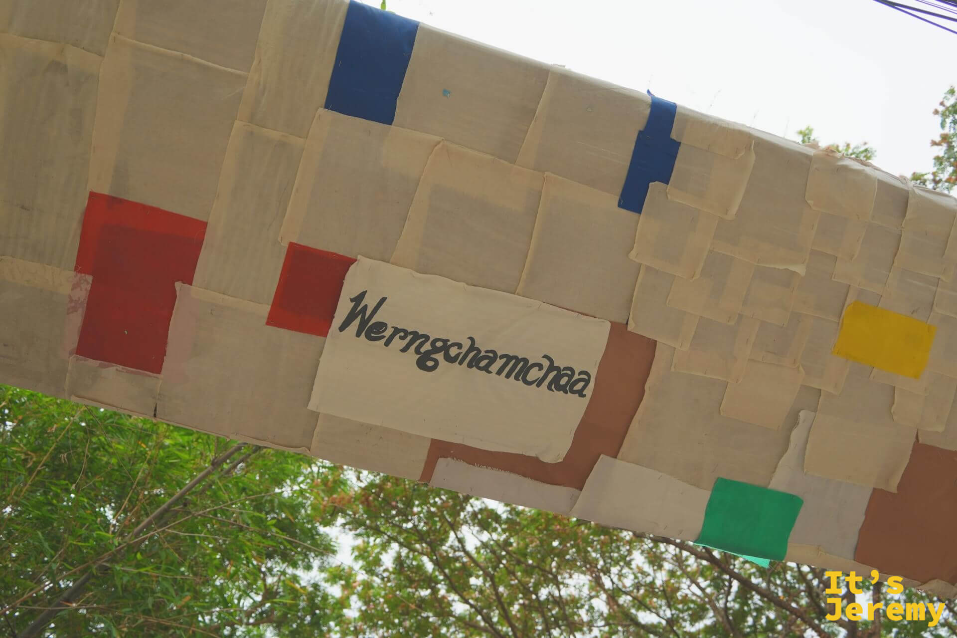 布拼貼牌樓近拍,米色布塊上縫著「Werngchamchaa」字樣與紅黃藍綠色塊