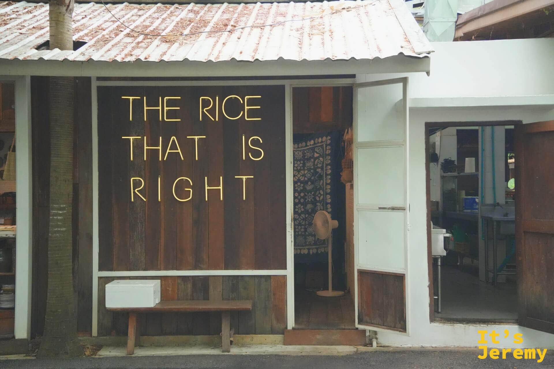 木牆上的黃色霓虹燈字「THE RICE THAT IS RIGHT」，旁邊門內掛著藍染布簾