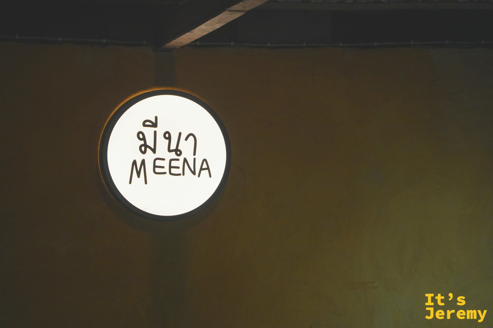 Meena 的圓形燈箱招牌，白底寫著泰文 มีนา 與英文 MEENA