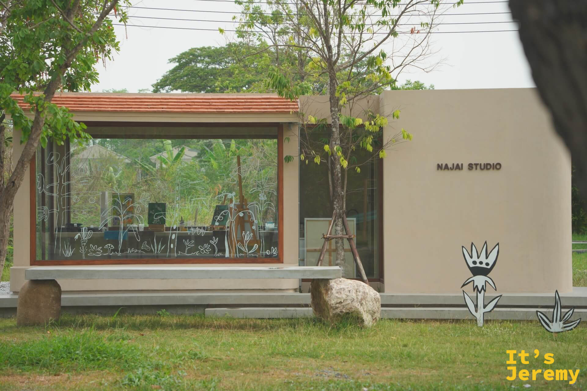 NAJAI STUDIO 的水泥建築外觀,大面落地窗上畫著插畫線條,門口立著黑白花朵剪板