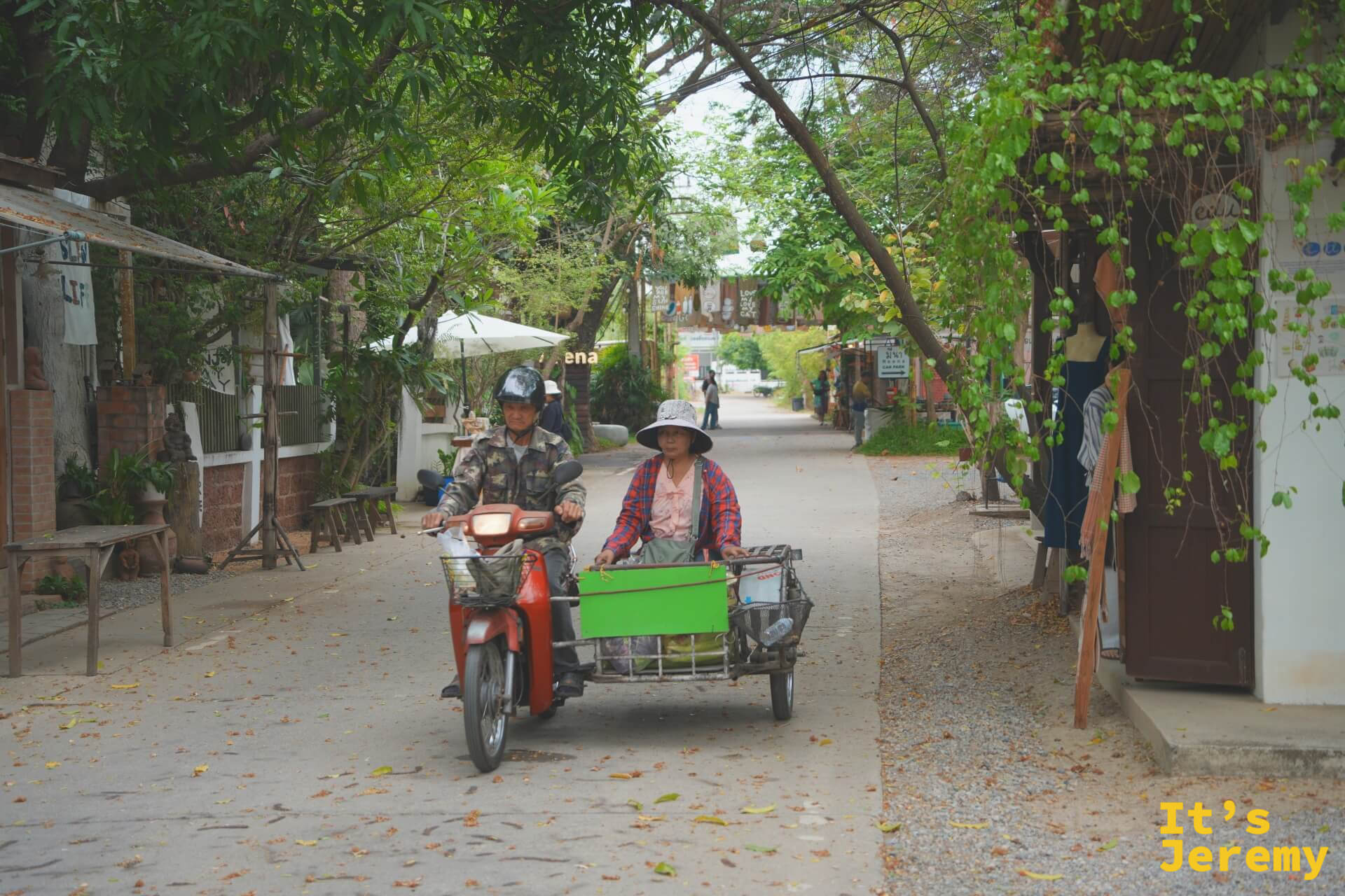 載貨三輪摩托車駛過市集主街,戴斗笠的攤販大姐坐在側斗裡