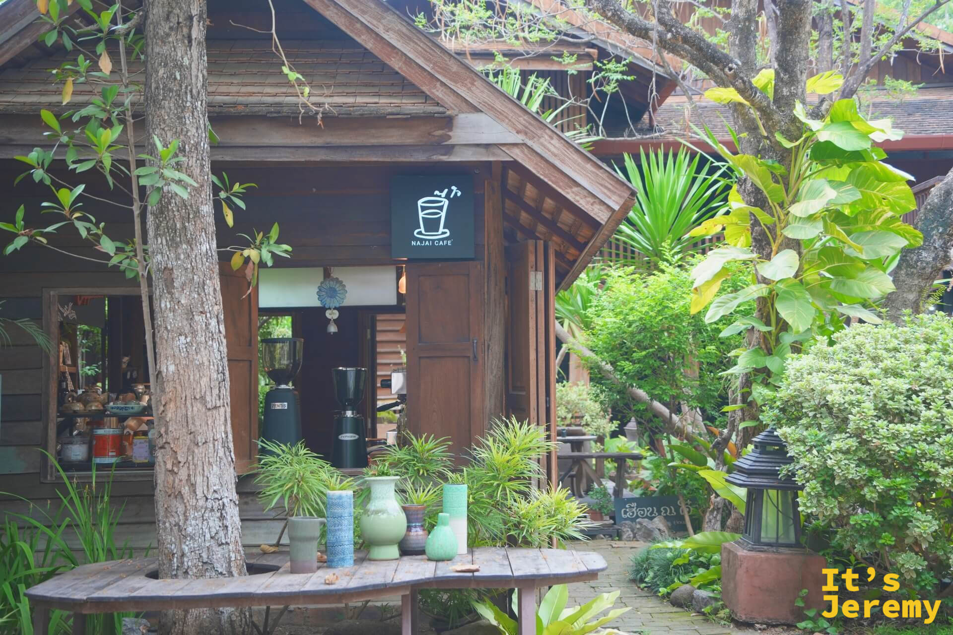 NAJAI CAFE 的老木屋店面,門口長桌上擺著綠色陶花瓶,被植物包圍