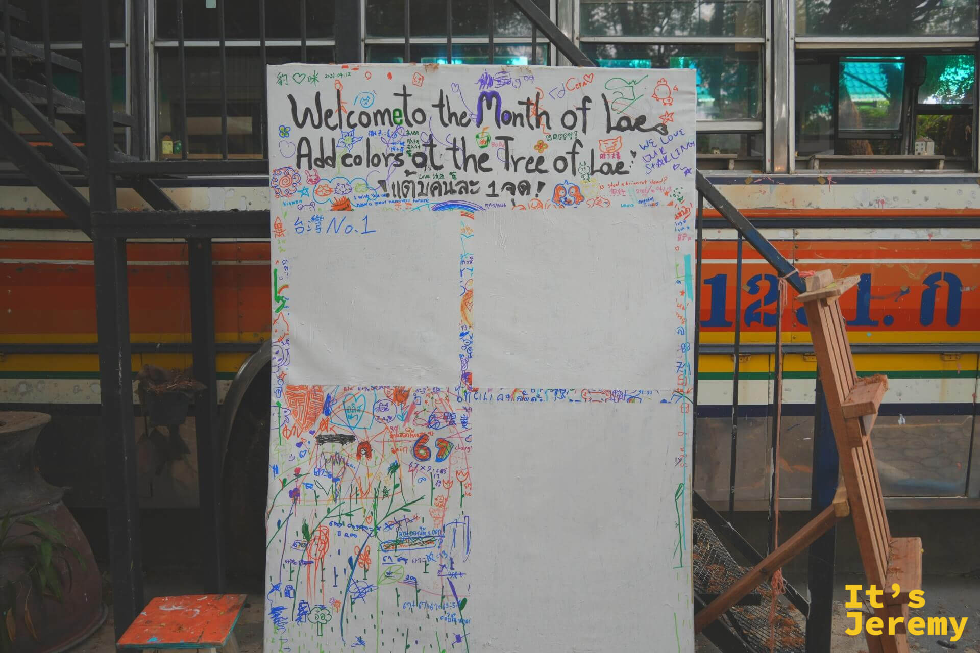 彩色巴士前的白色留言塗鴉板,寫著「Welcome to the Month of Lae, Add colors at the Tree of Lae」,畫滿各色塗鴉
