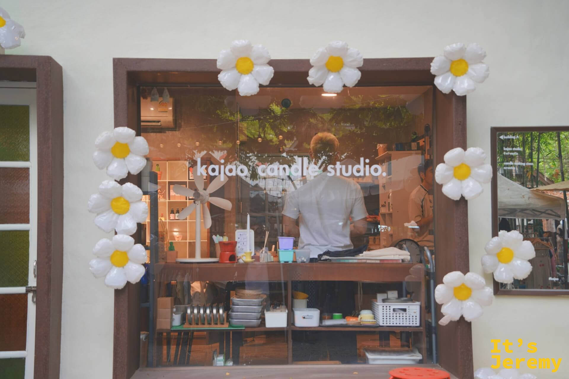 kajao candle studio 的工作室窗口,木窗框四周裝飾白色雛菊氣球,店員在裡面備料