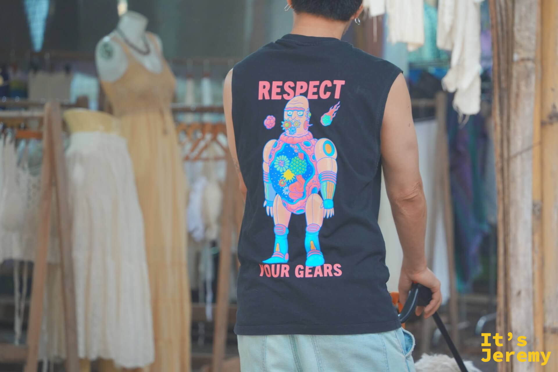 穿著「RESPECT YOUR GEARS」插畫背心的男子背影,前方是掛滿棉麻洋裝的服飾攤